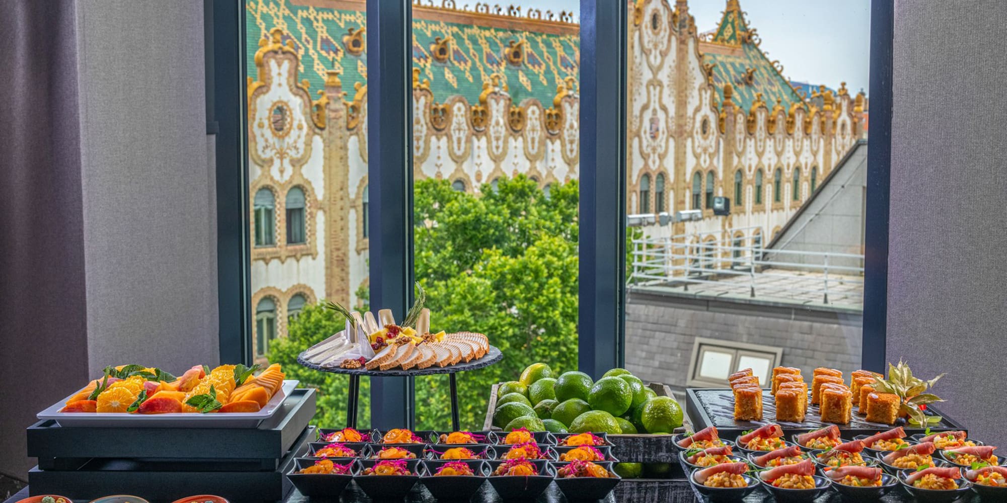Appetizer buffet with fresh fruit, small bites, and historic building window view.