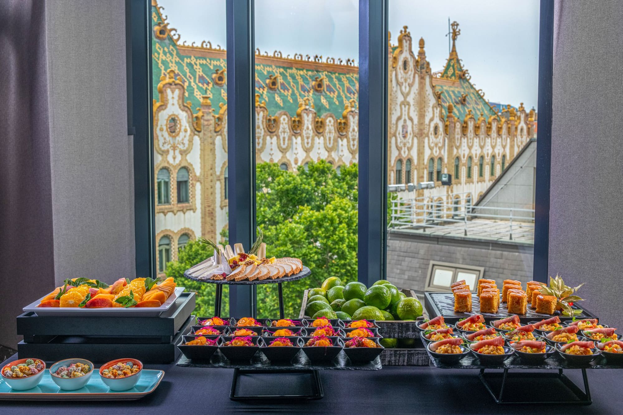 Appetizer buffet with fresh fruit, small bites, and historic building window view.