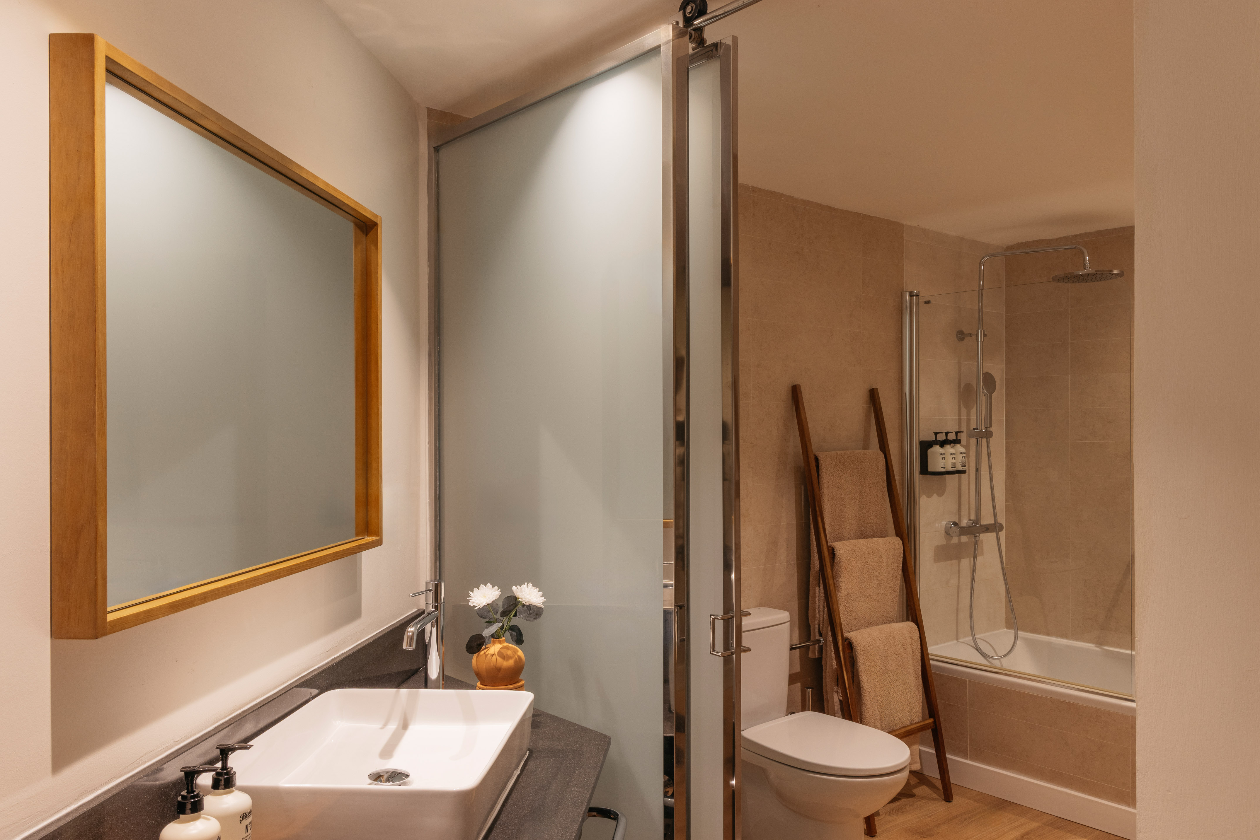 Bathroom with white sink, wooden mirror, frosted glass door, toilet, and shower.