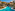 Luxury resort swimming pool with bridge, palm trees, and terraced hotel buildings.