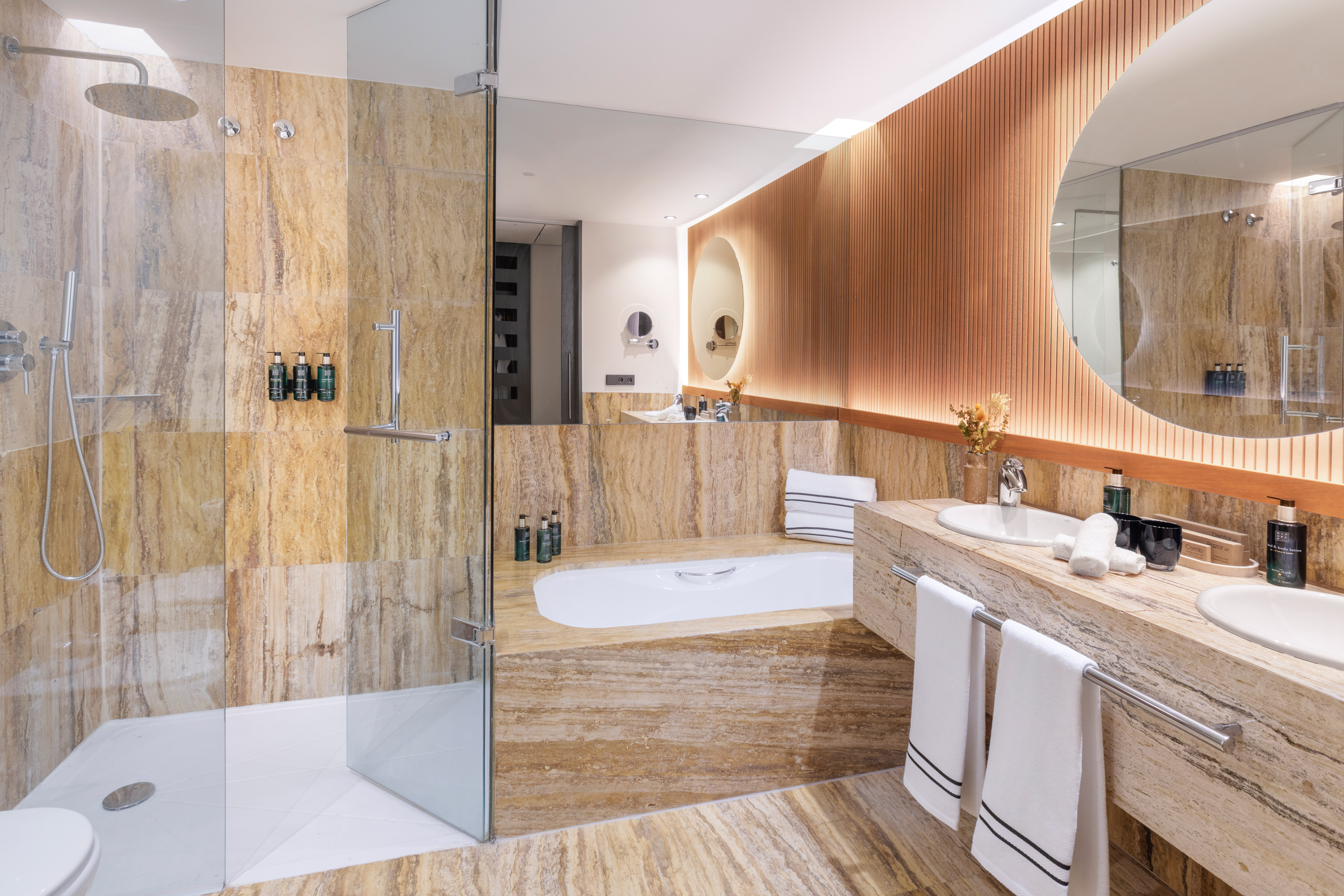 Luxury hotel bathroom: travertine, walk-in shower, bathtub, double vanity.