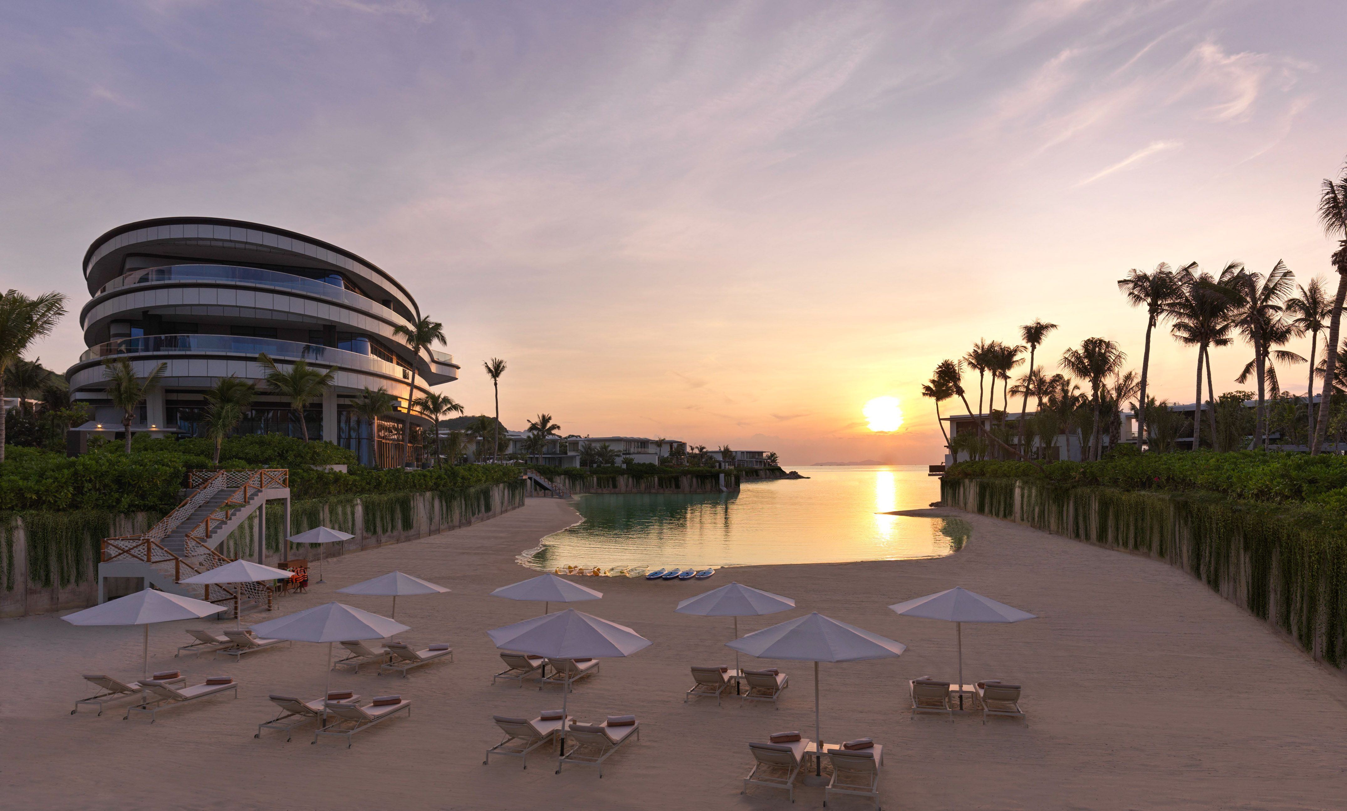 Luxury beach resort sunset: modern hotel, sandy beach, umbrellas, calm ocean.