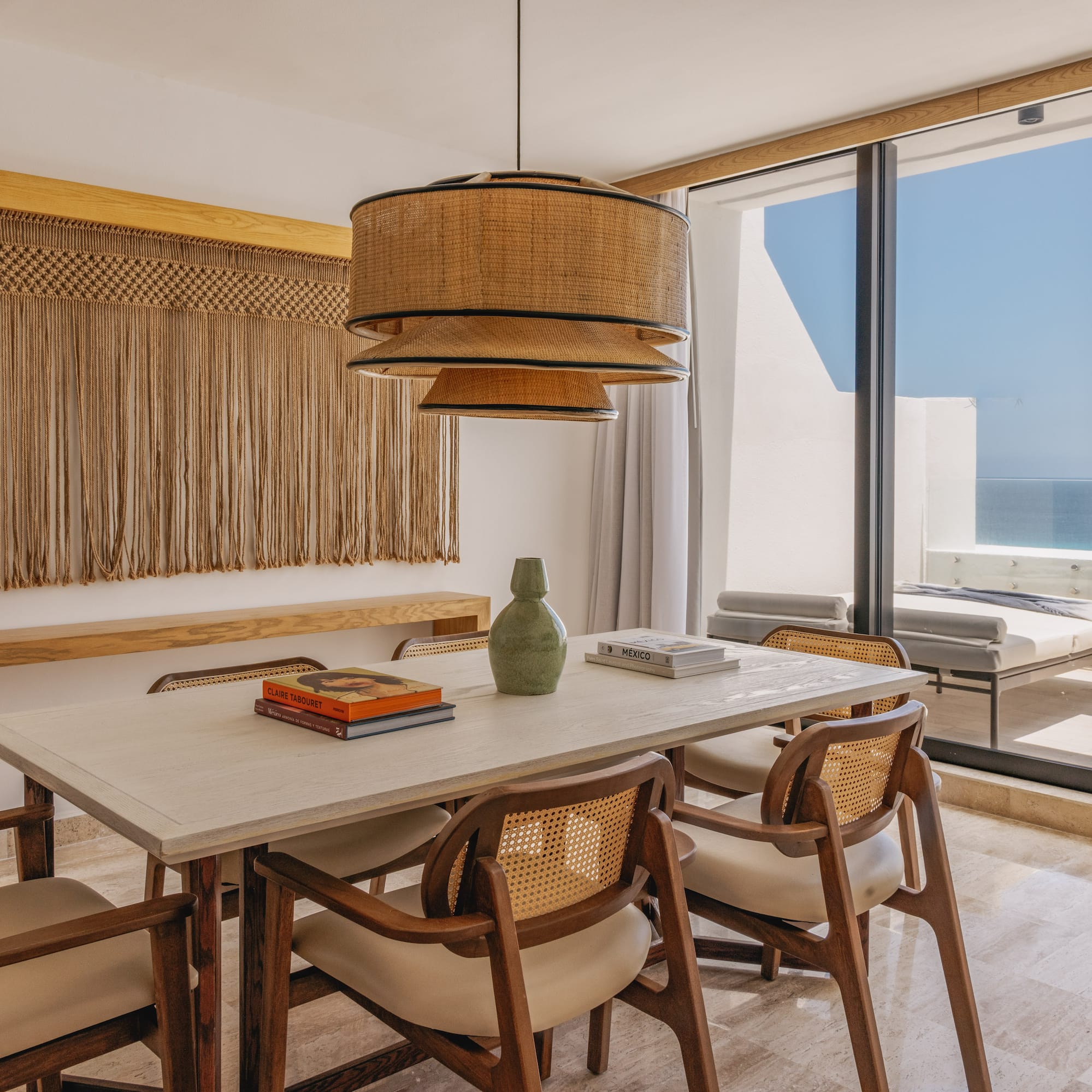 Dining room with ocean view, rattan pendant, macrame, and wooden chairs.