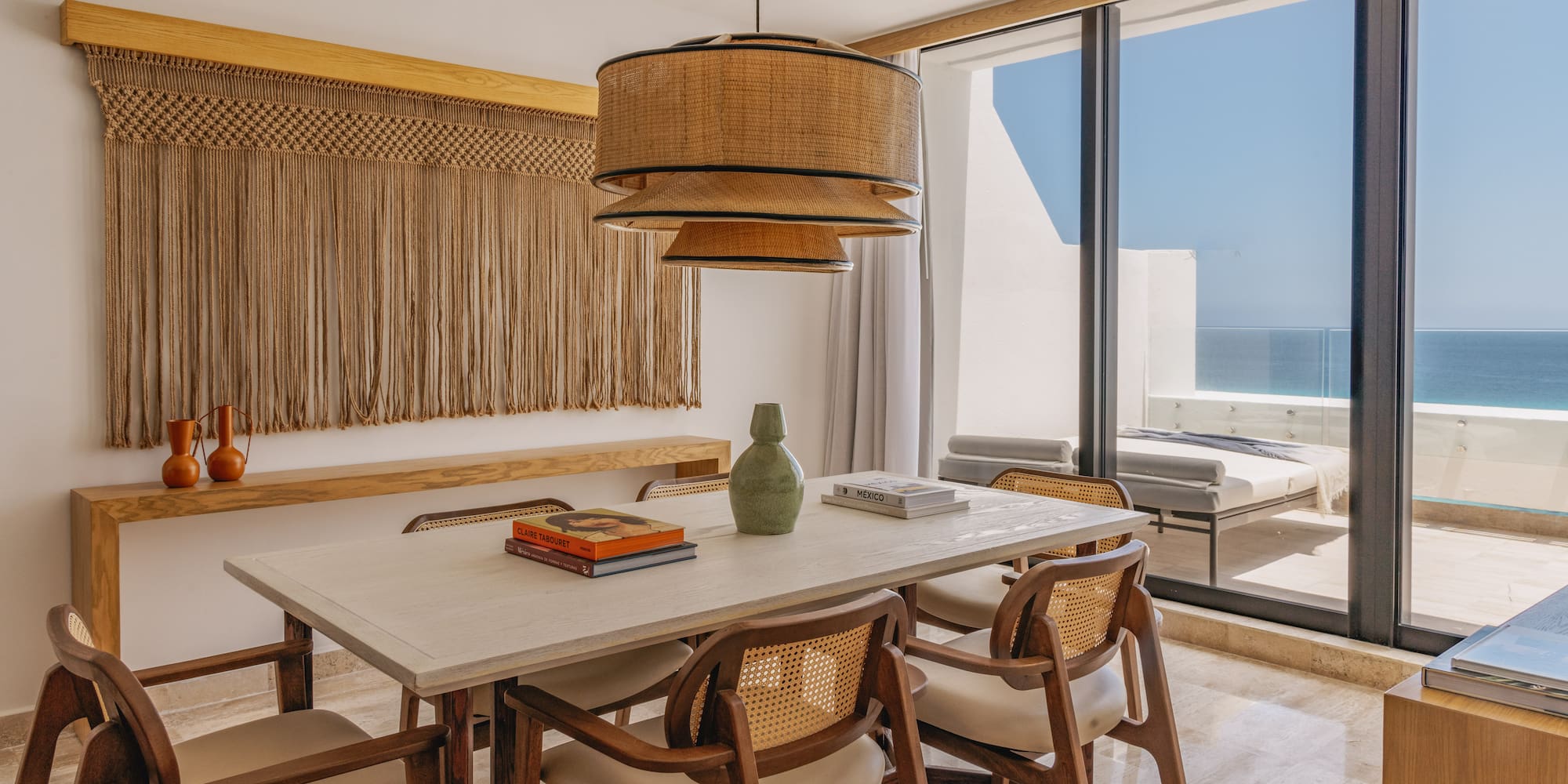 Dining room with ocean view, rattan pendant, macrame, and wooden chairs.