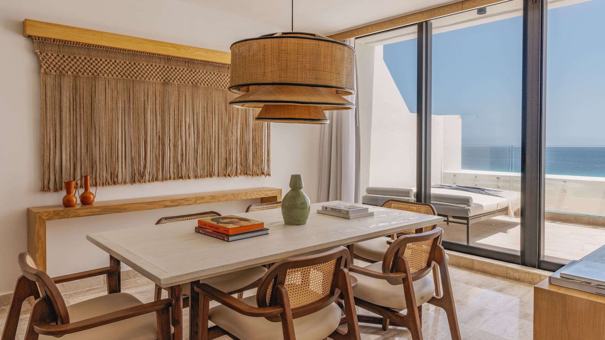 Dining room with ocean view, rattan pendant, macrame, and wooden chairs.
