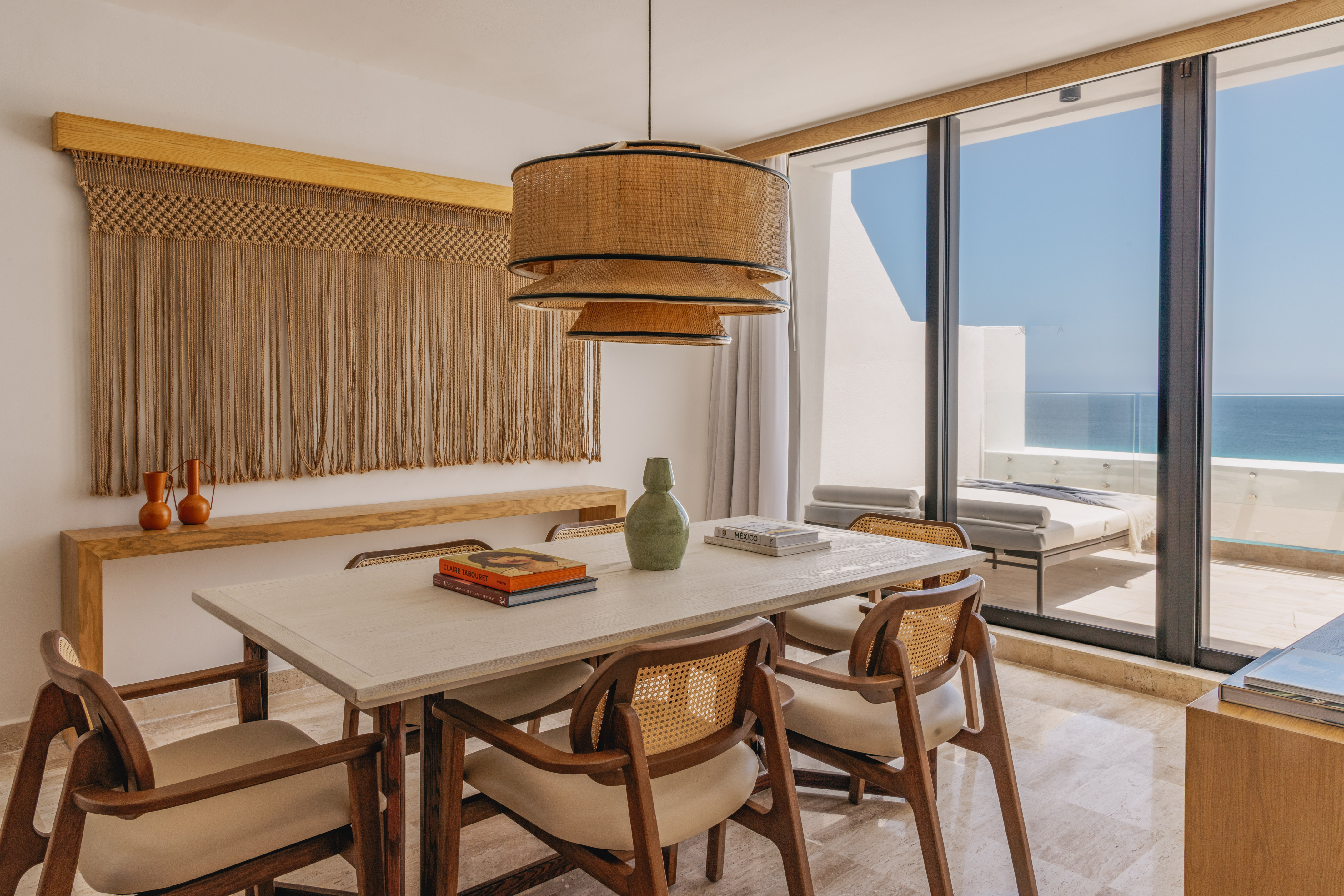 Dining room with ocean view, rattan pendant, macrame, and wooden chairs.
