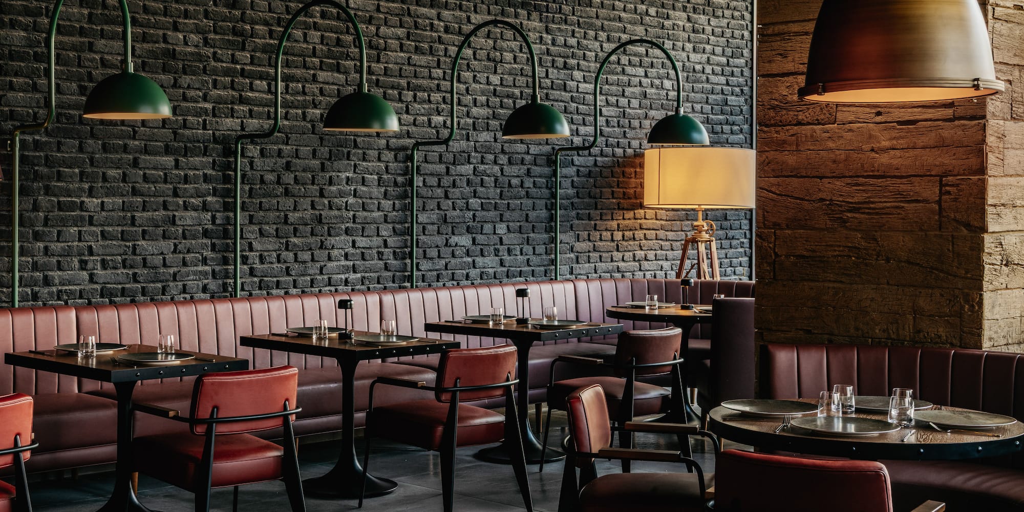 Restaurant dining room: black brick wall, red leather booths, green pendant lamps.