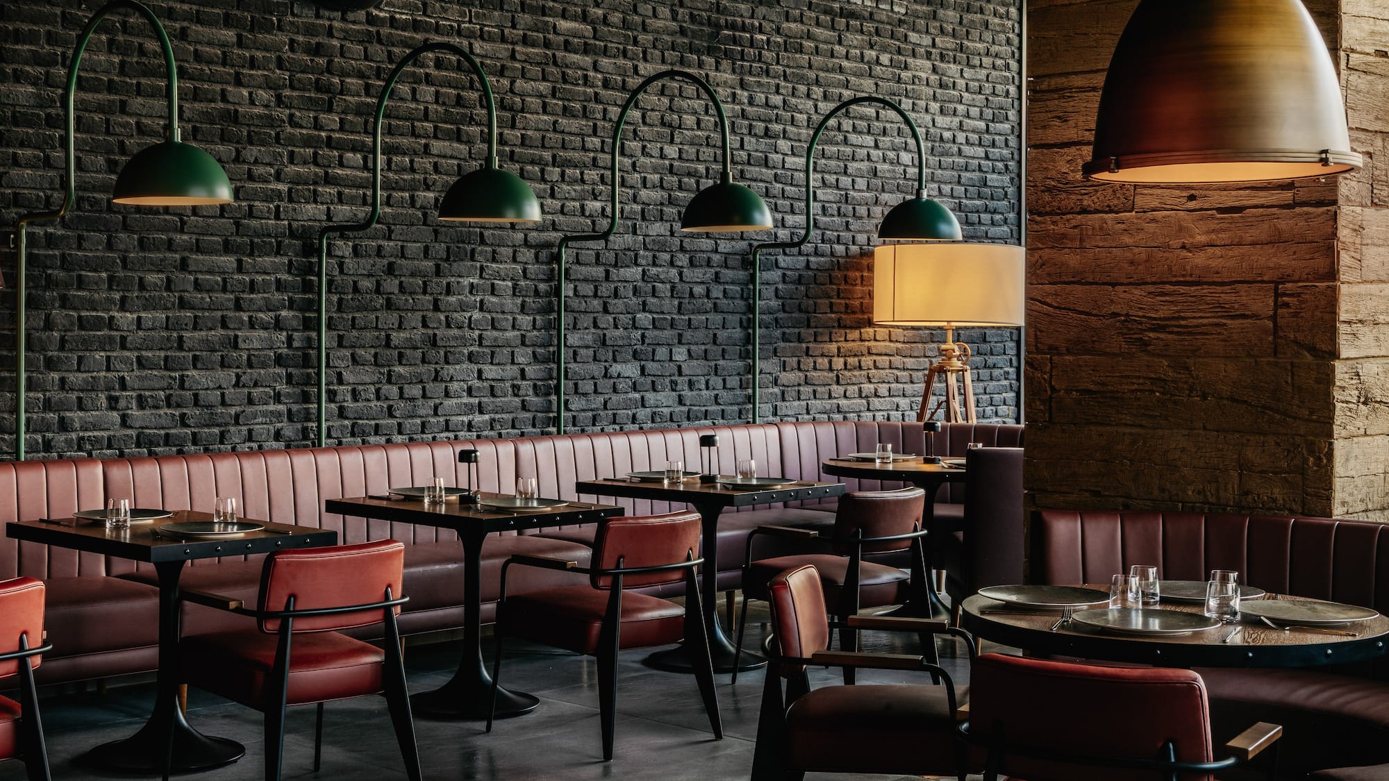 Restaurant dining room: black brick wall, red leather booths, green pendant lamps.