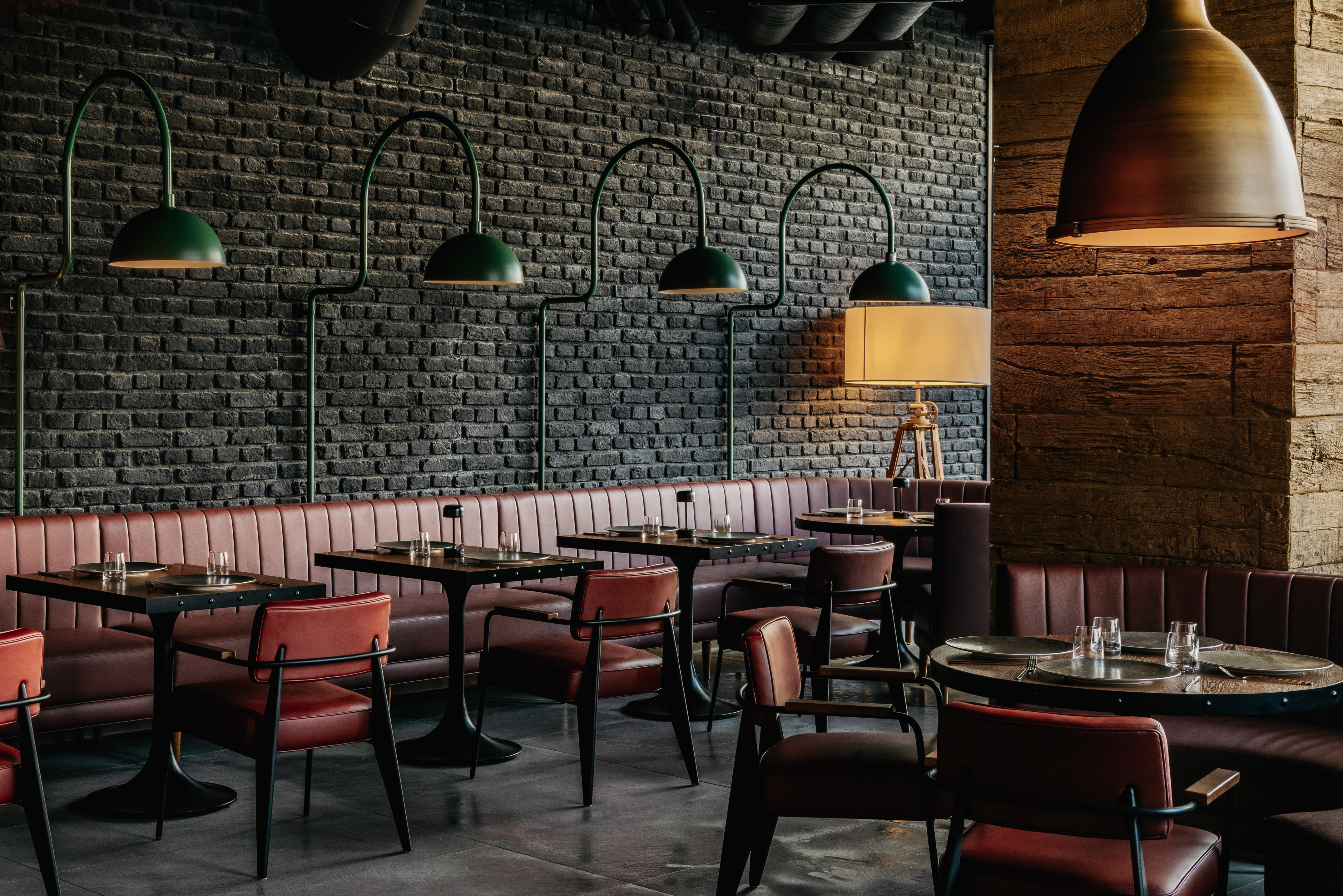 Restaurant dining room: black brick wall, red leather booths, green pendant lamps.