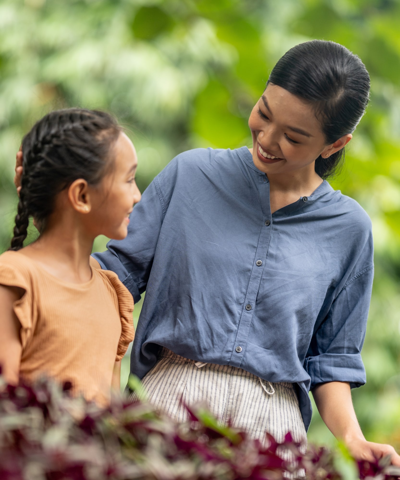 Smiling mother and daughter embracing outdoors, green foliage background.