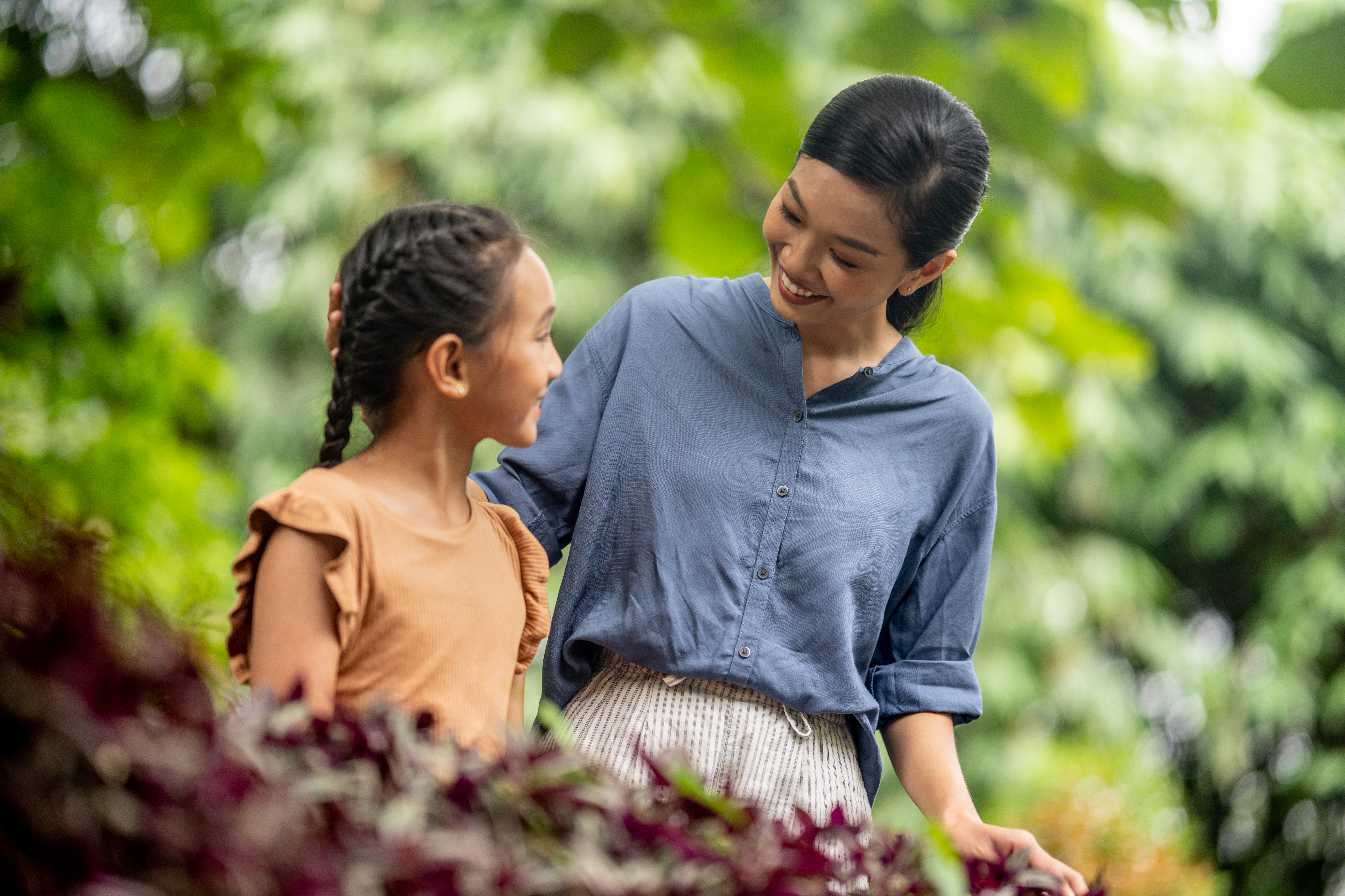 Smiling mother and daughter embracing outdoors, green foliage background.