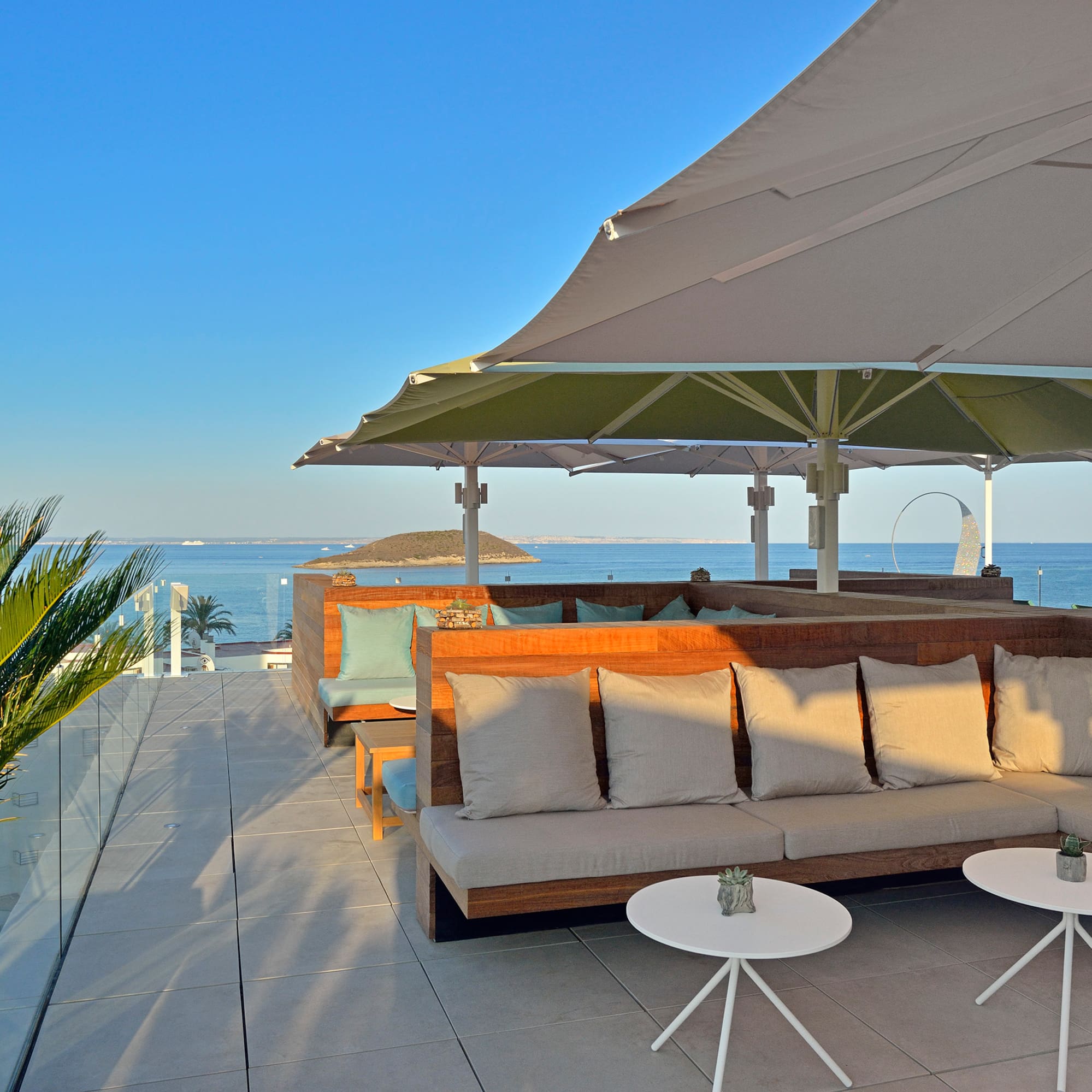 Resort rooftop terrace with ocean view, modern outdoor lounge seating, and sun umbrellas.