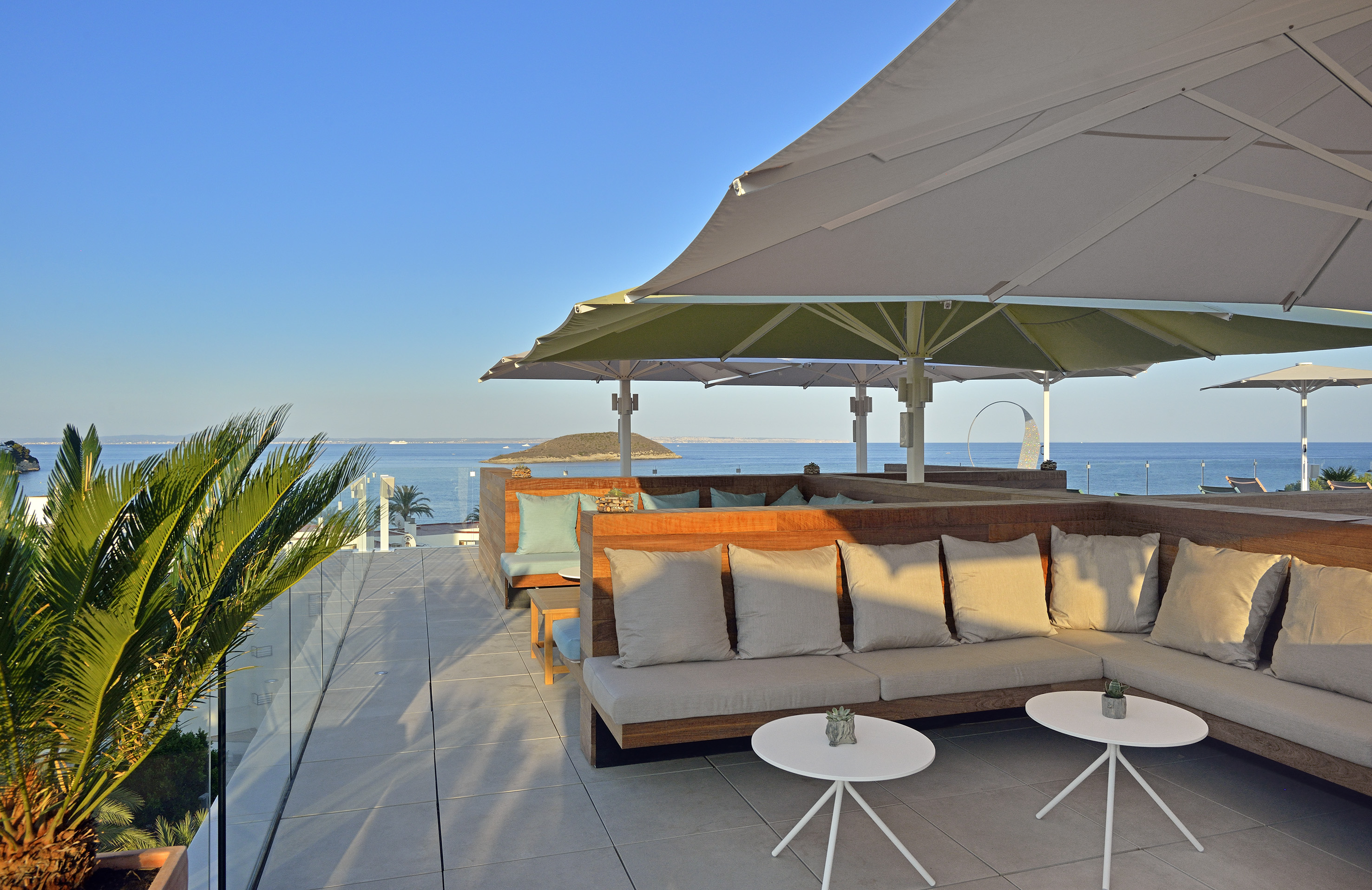 Resort rooftop terrace with ocean view, modern outdoor lounge seating, and sun umbrellas.
