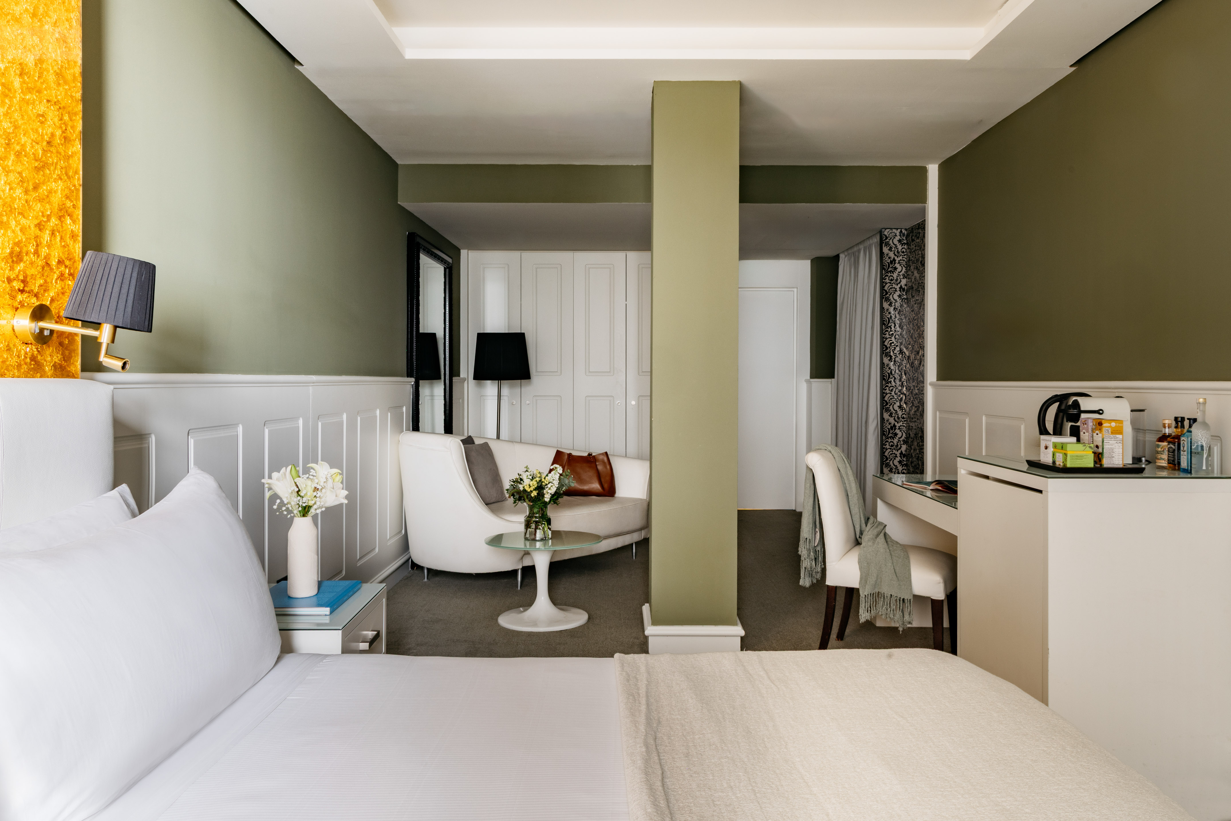 Modern hotel room with white bed, olive green walls, curved sofa, and workspace.