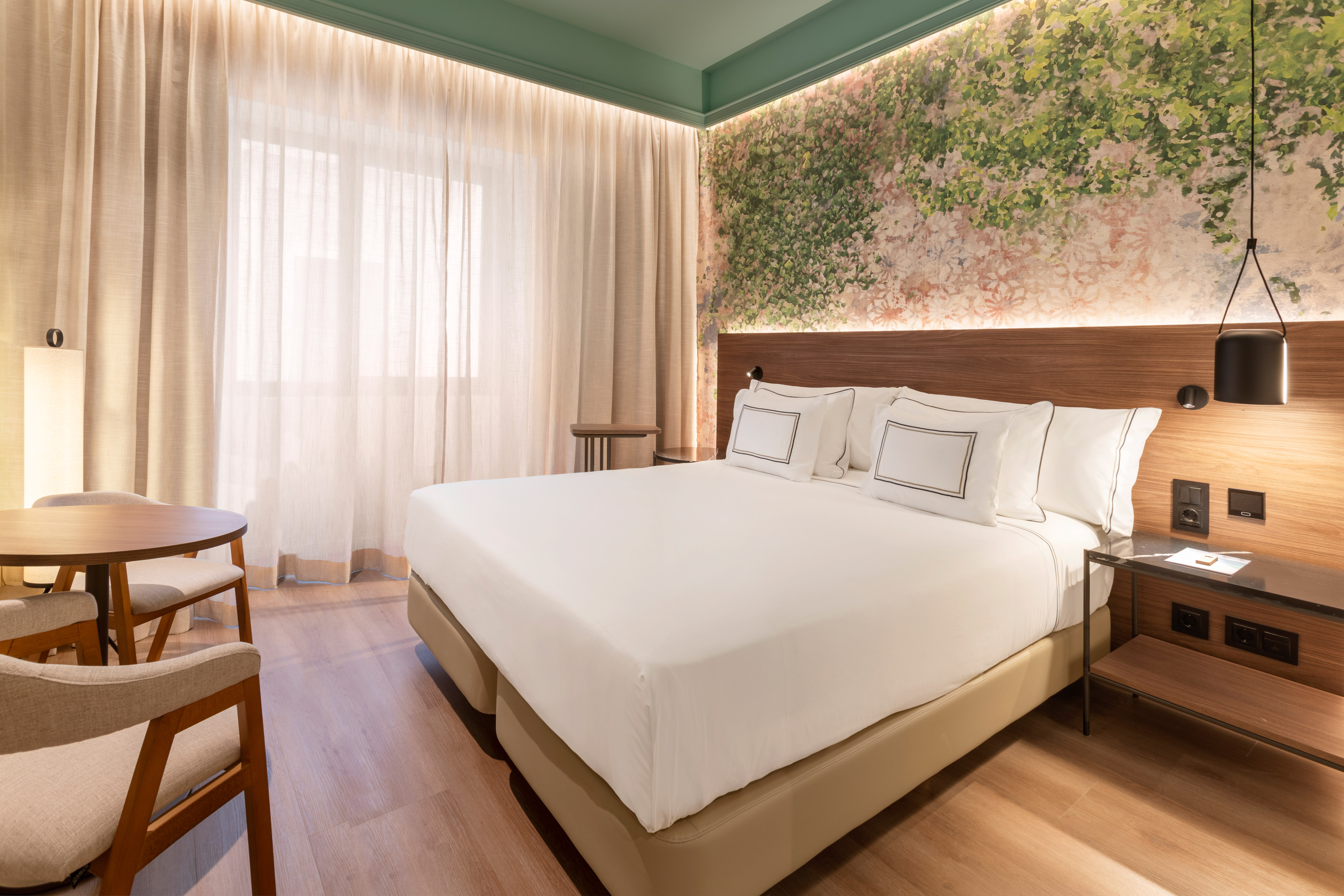Modern hotel room with large bed, botanical wall decor, and cozy seating.