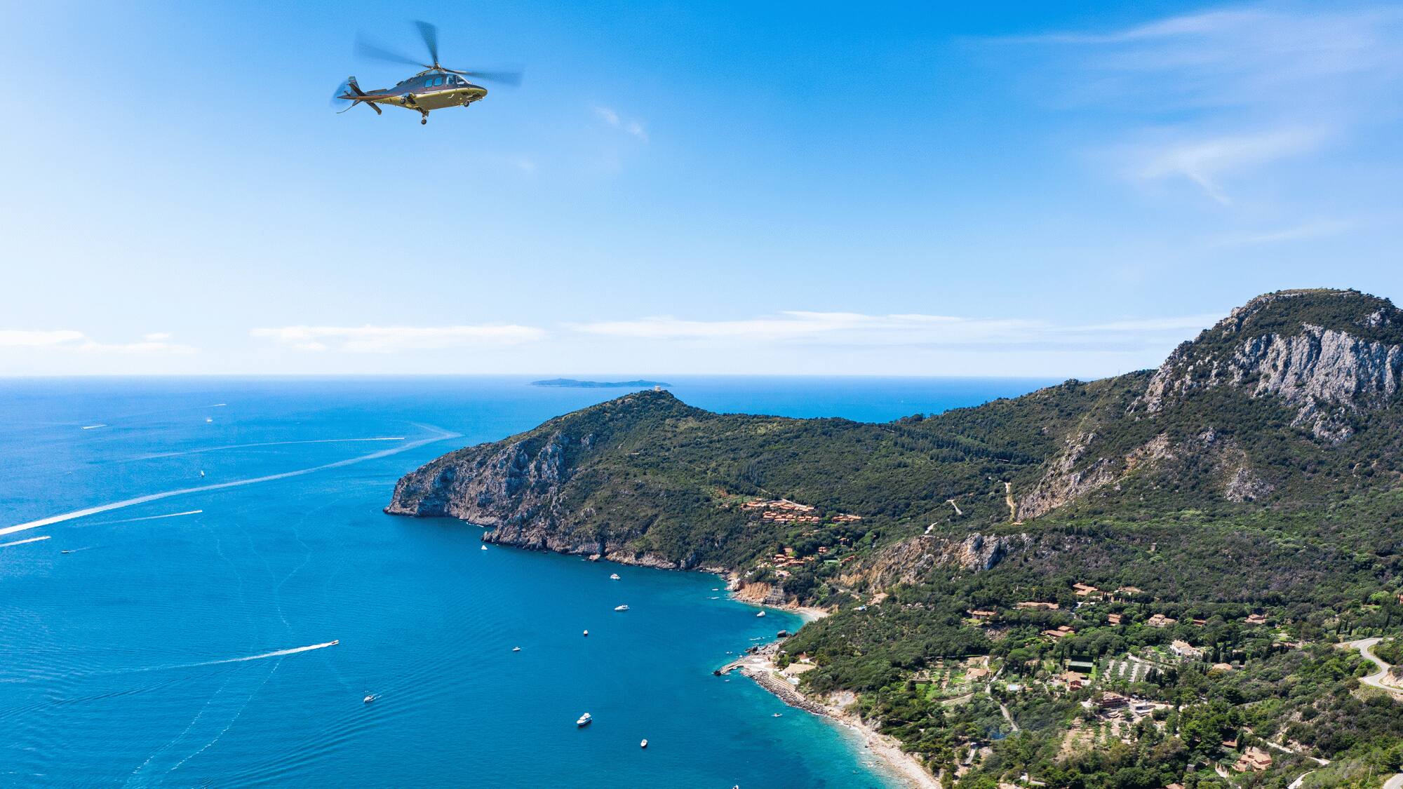 Helicopter aerial view of blue sea, green coastal mountains, and boats.