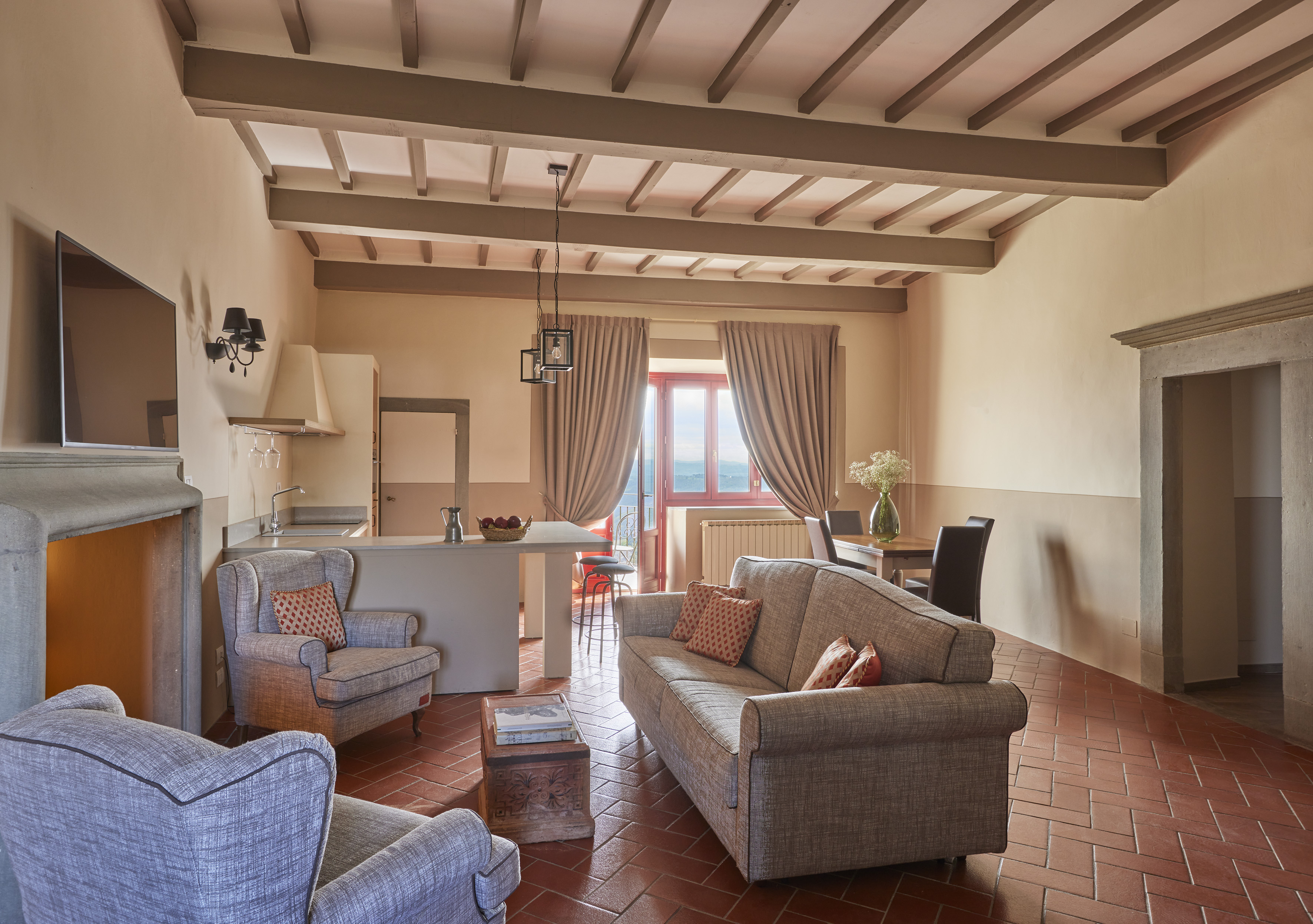 Tuscan living room with terracotta floor, exposed beams, and open kitchen.