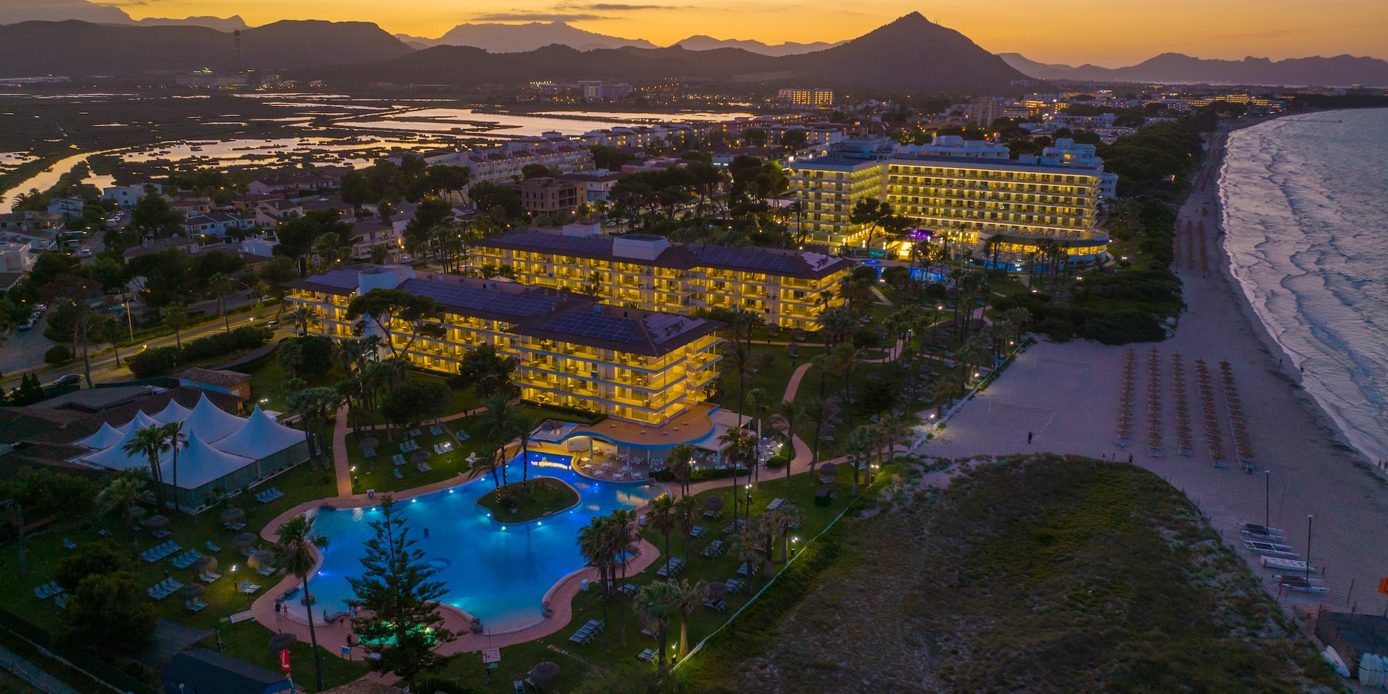 a hotel with a pool and a beach at sunset