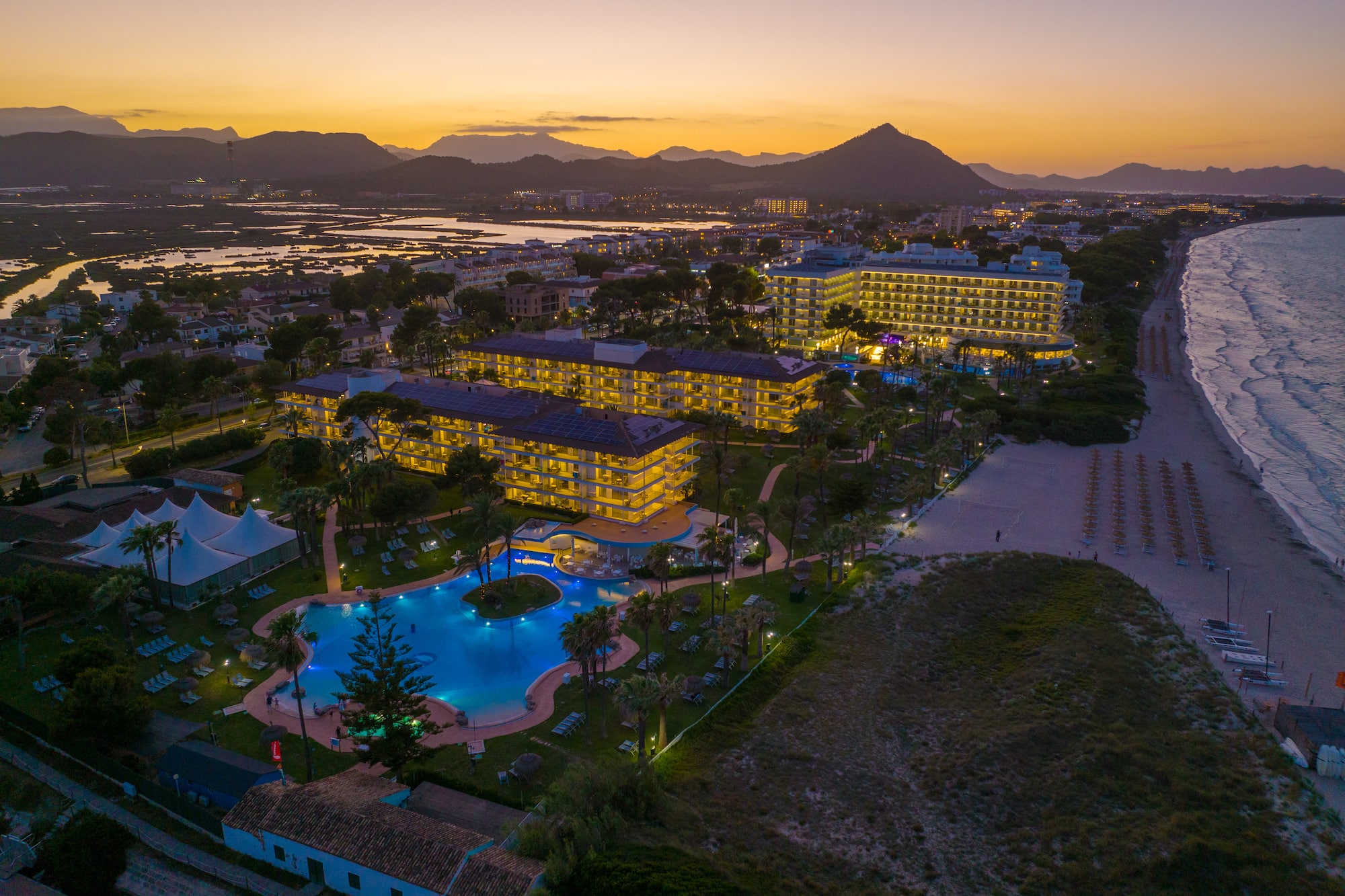 a hotel with a pool and a beach at sunset