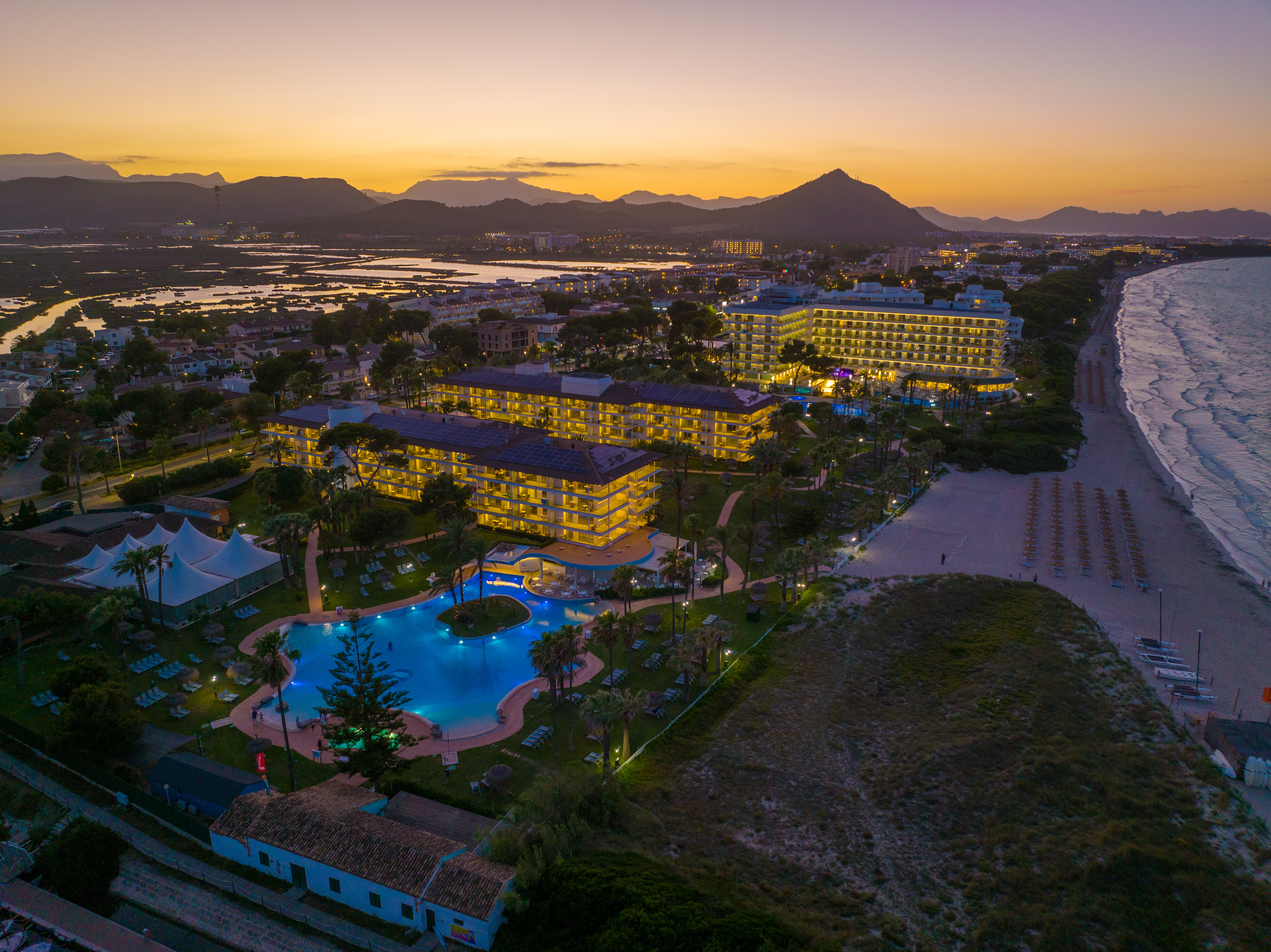 a hotel with a pool and a beach at sunset