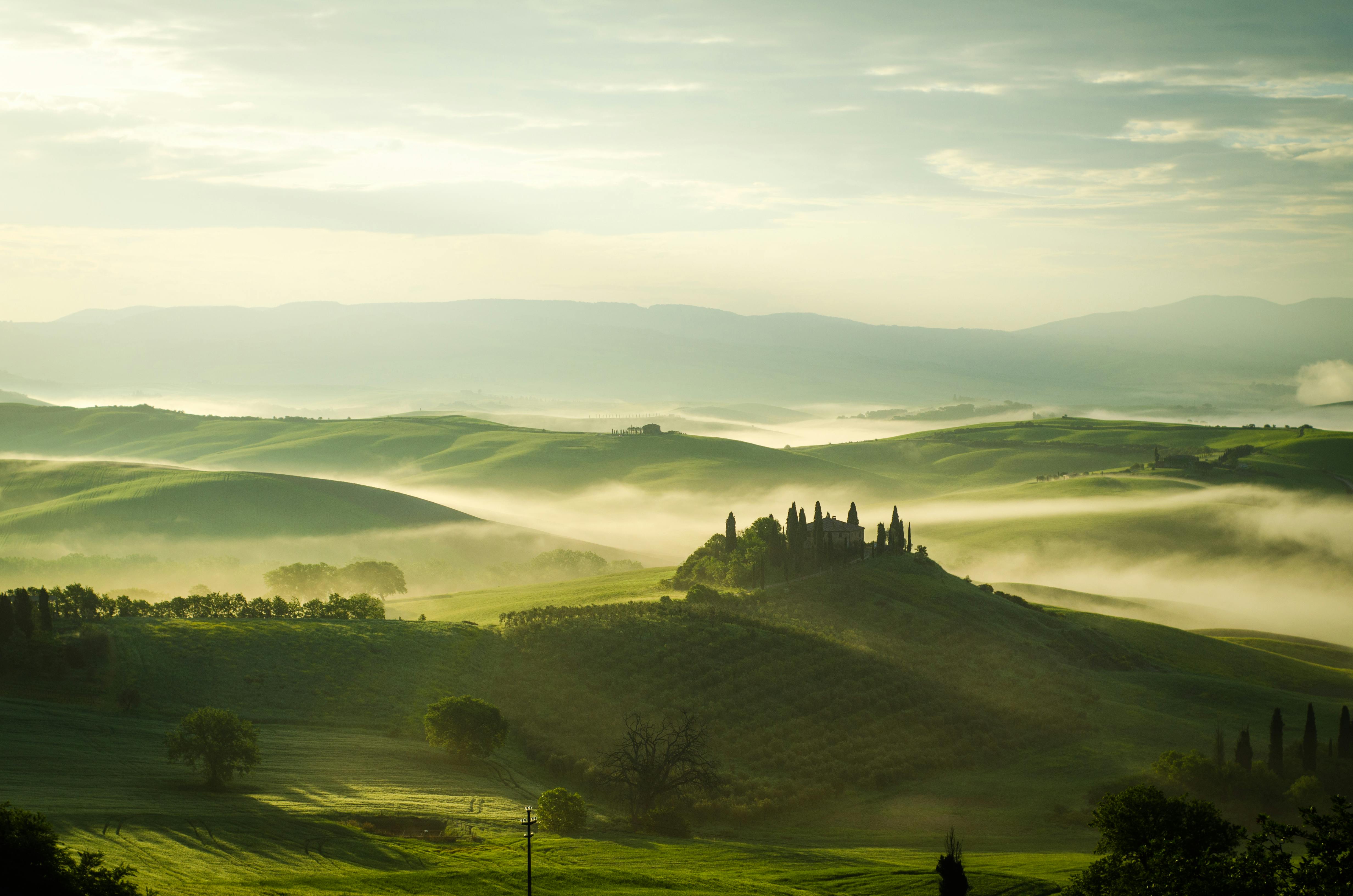 Sunrise over foggy Tuscan hills, with a historic villa and cypress trees.
