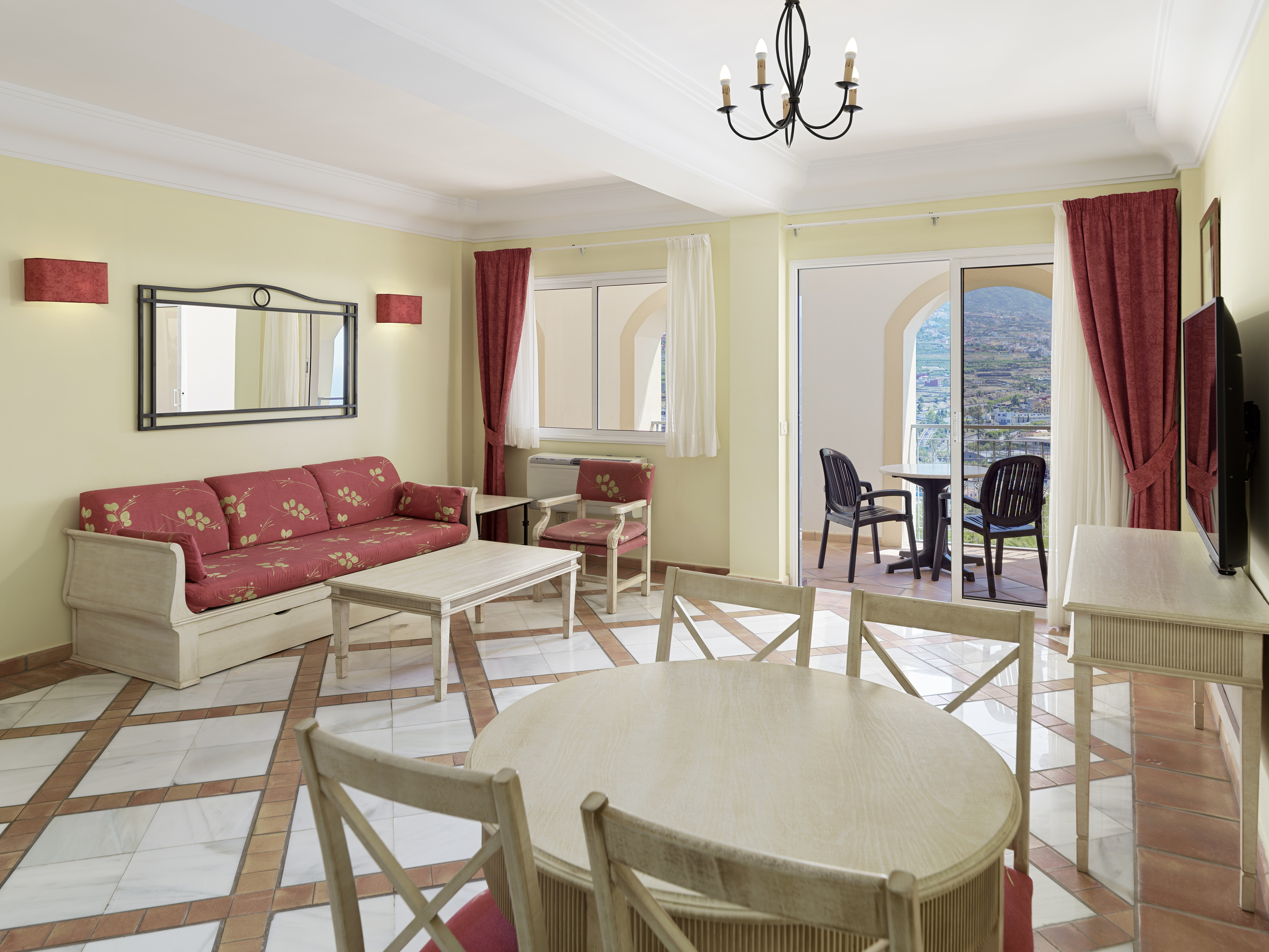 Tiled living room with red sofa, dining table, and mountain view balcony.