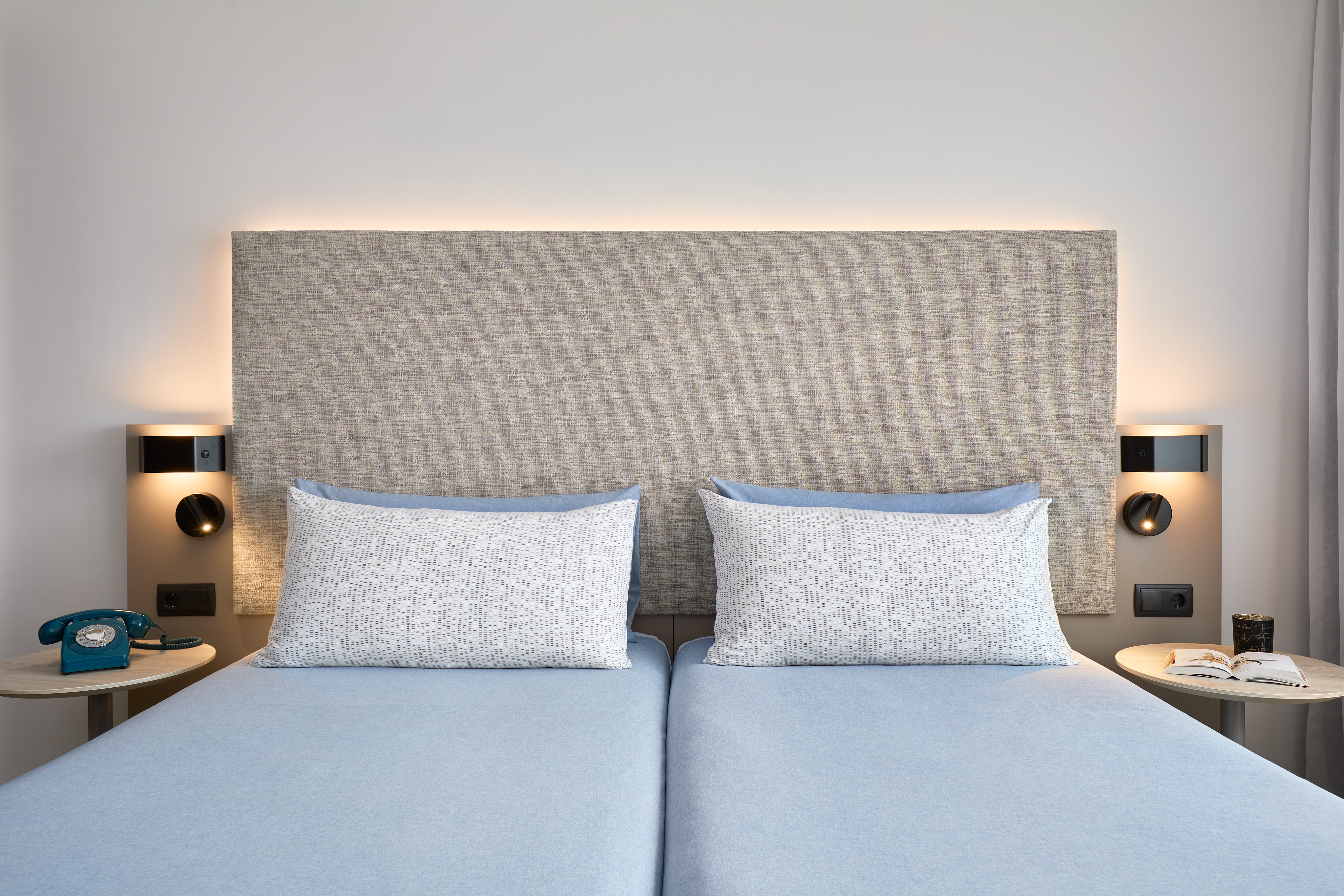 Modern hotel room: twin beds, lit fabric headboard, bedside tables.