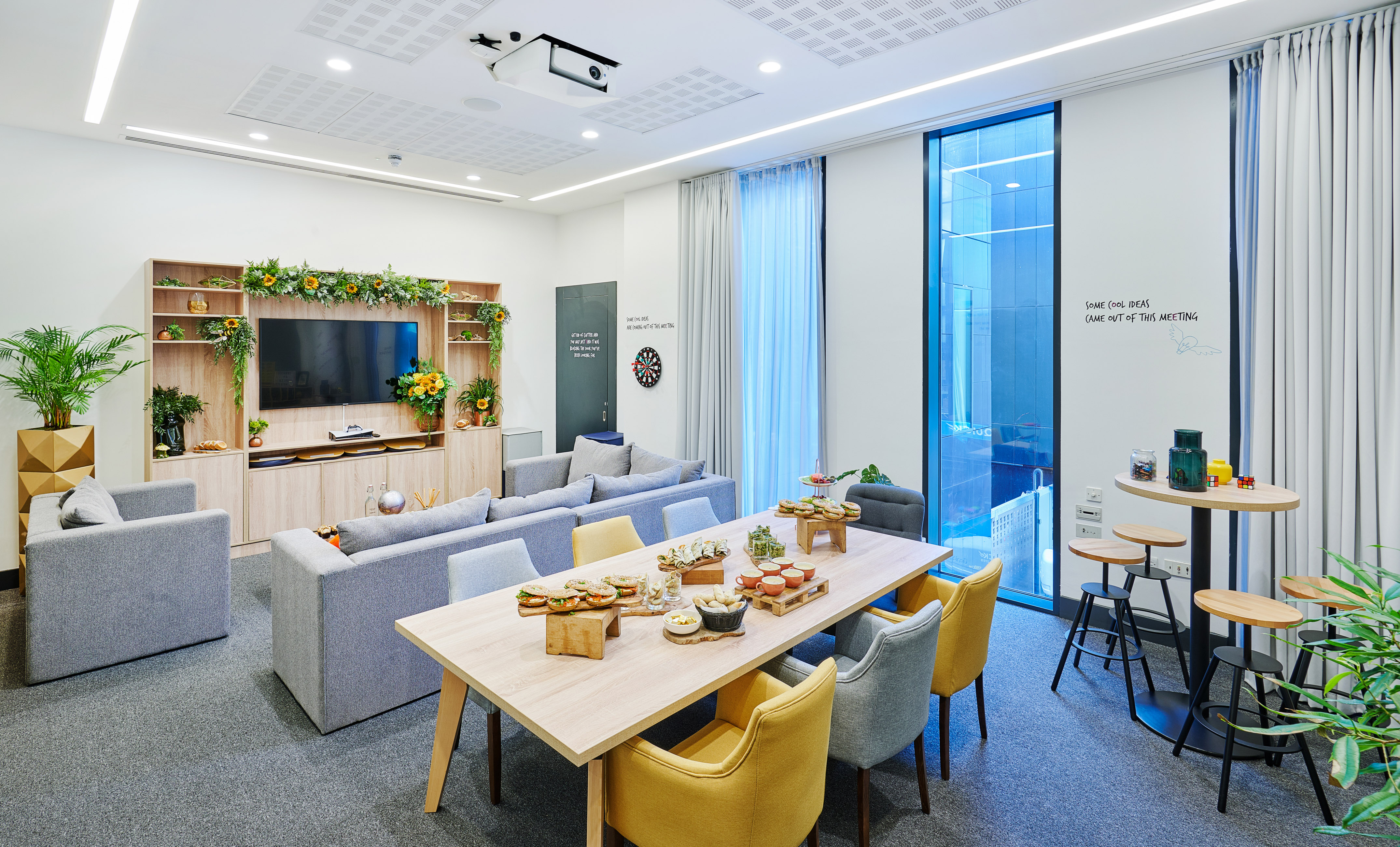 Modern office collaboration lounge with snacks, TV, projector, and comfortable seating.