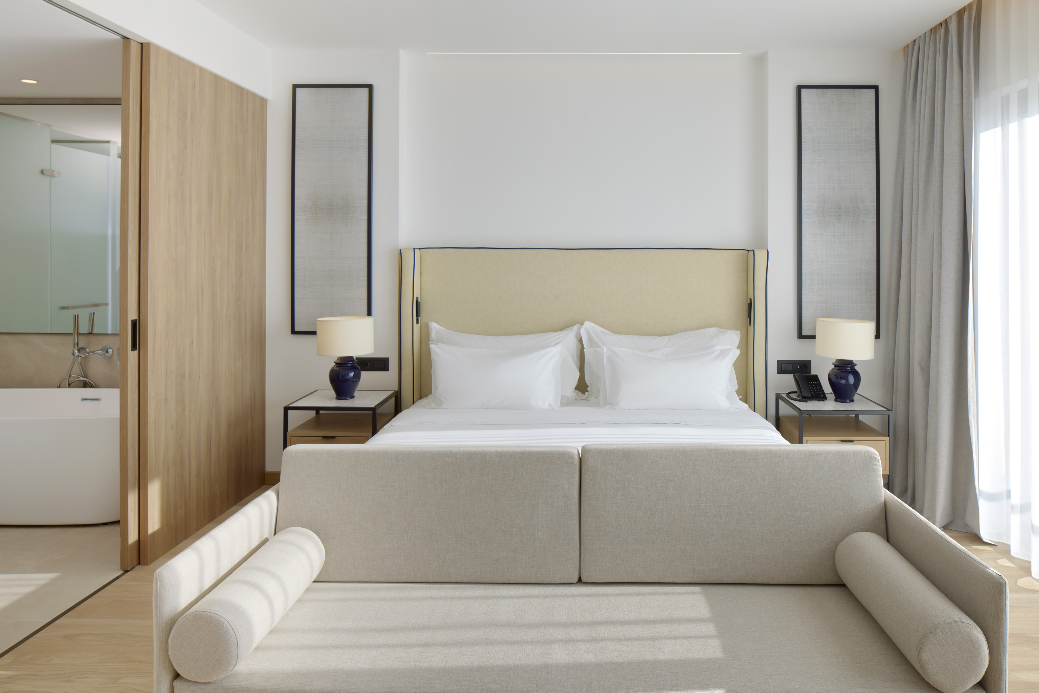 Modern hotel room with king bed, bench, and bathroom access.