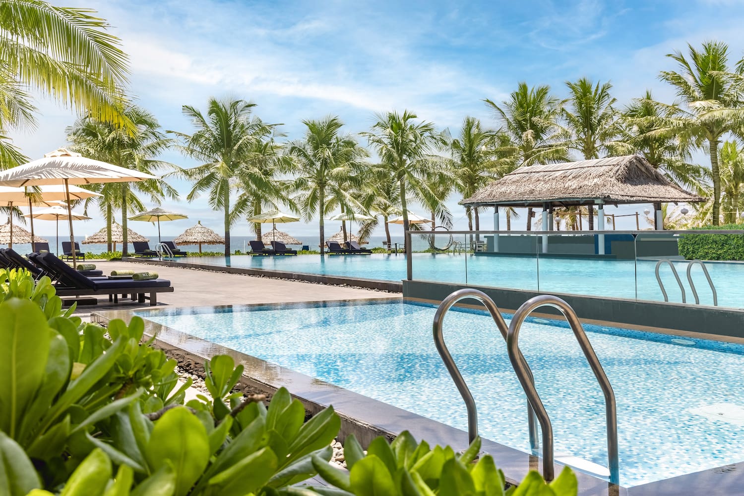 a pool with chairs and umbrellas by a beach