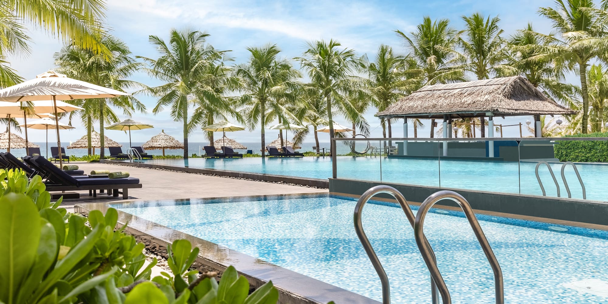 a pool with chairs and umbrellas by a beach