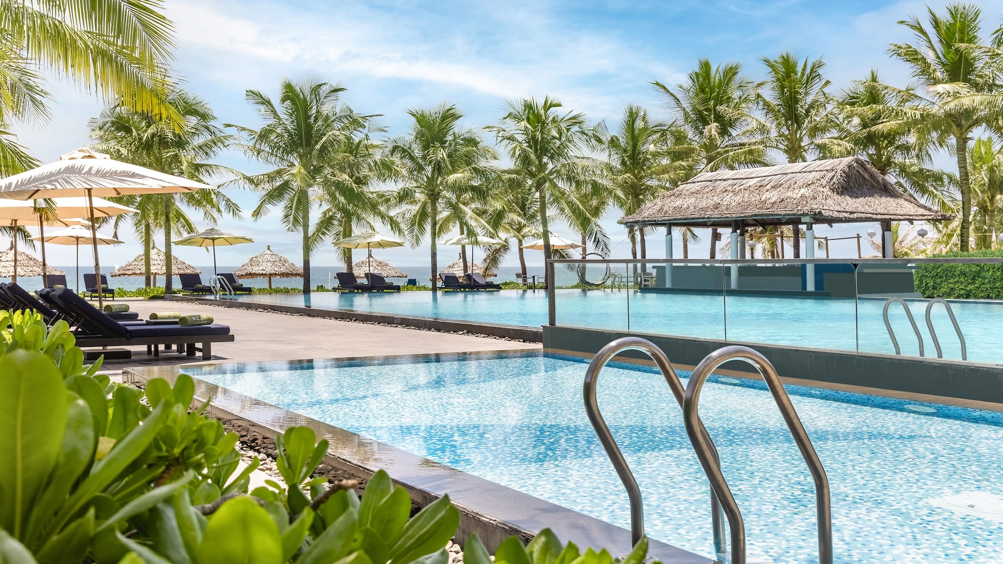 a pool with chairs and umbrellas by a beach