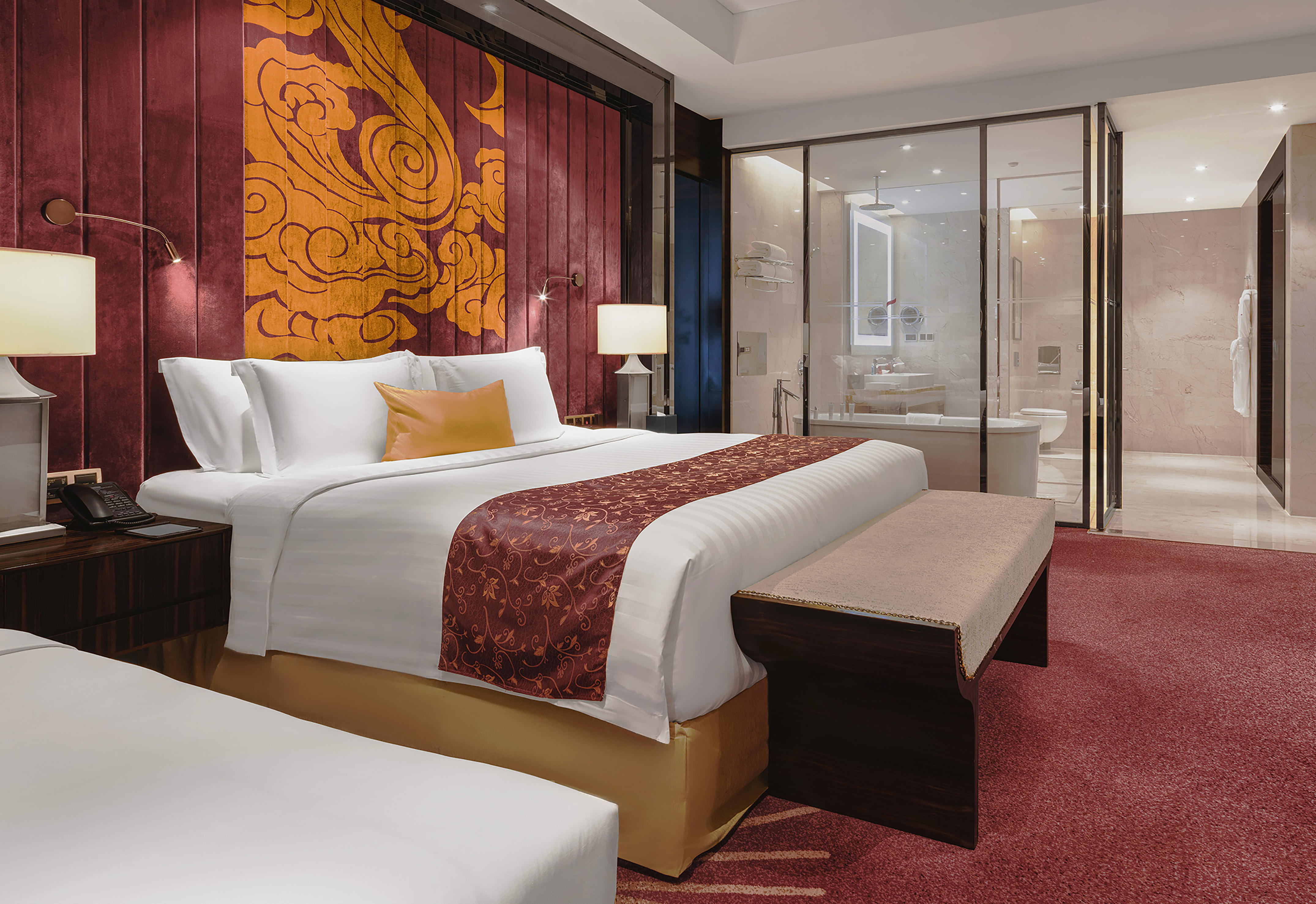 Luxury hotel bedroom with red and gold decor, modern design, and glass bathroom.