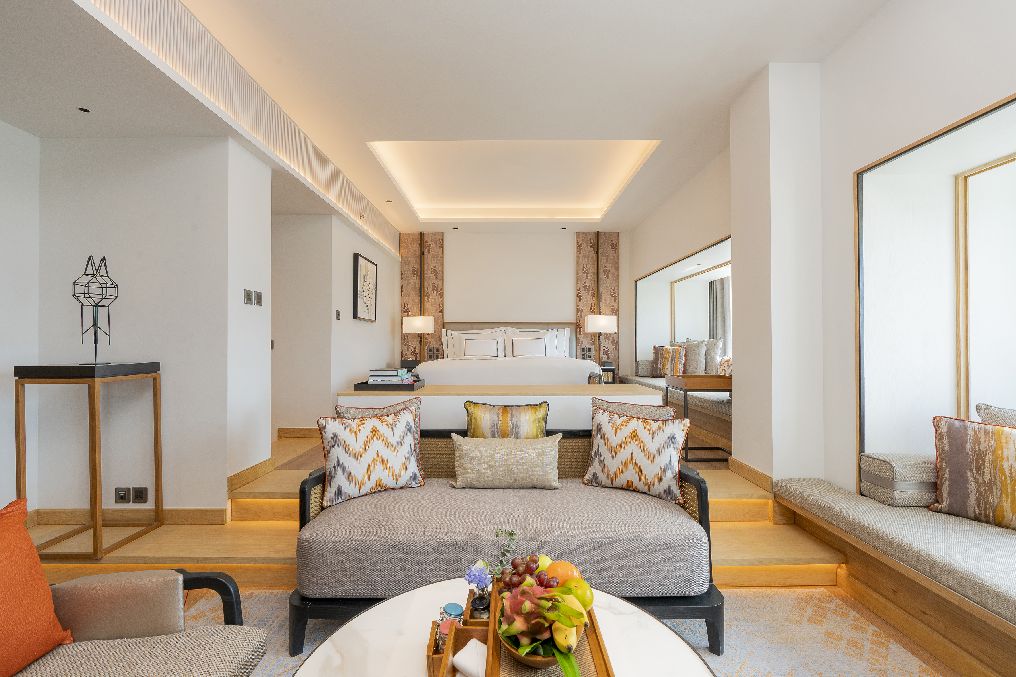 Luxury hotel suite with modern bed, lounge area, and fresh fruit platter.