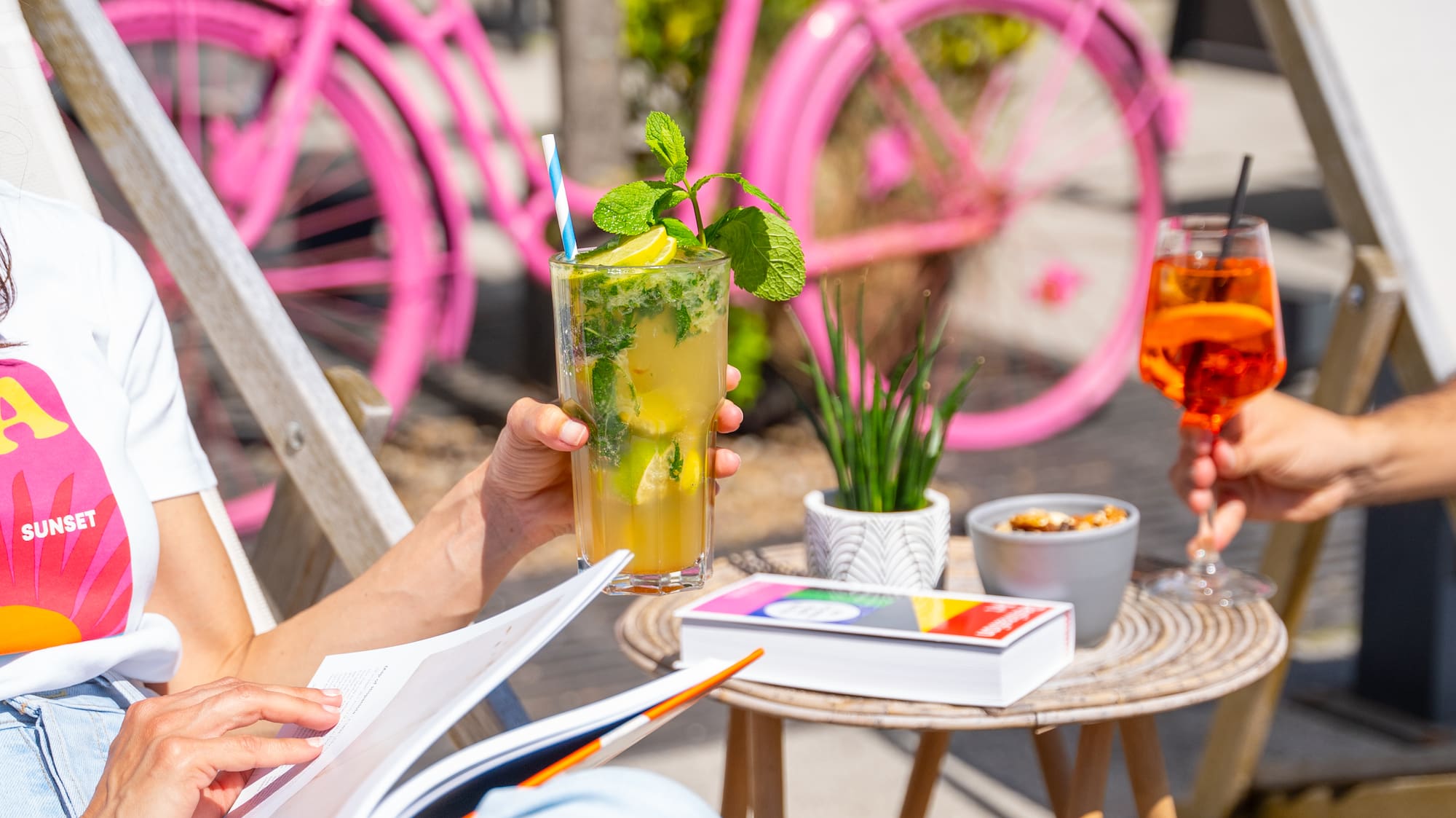 a woman sitting outside with a drink and a pink bicycle