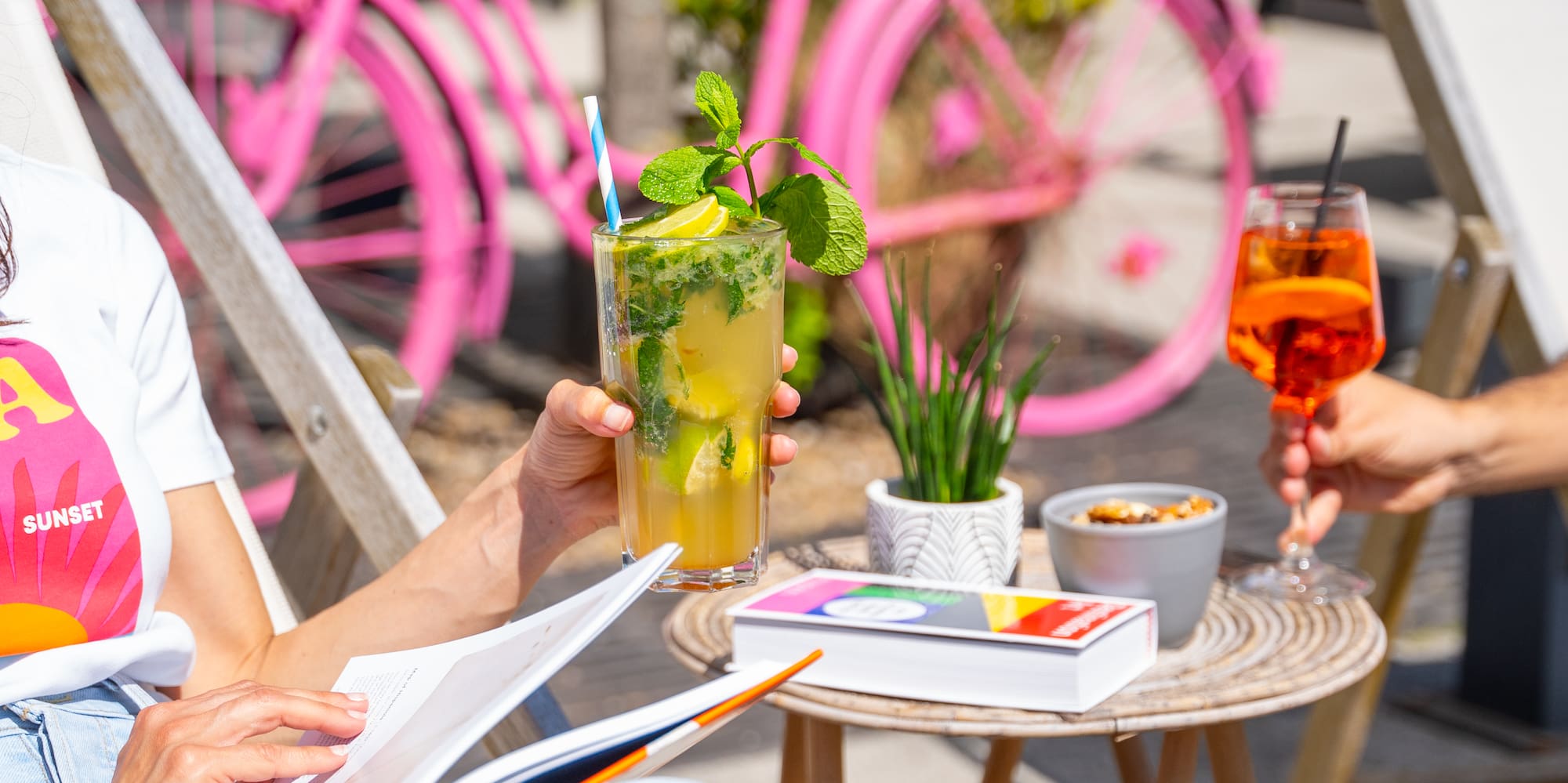 a woman sitting outside with a drink and a pink bicycle