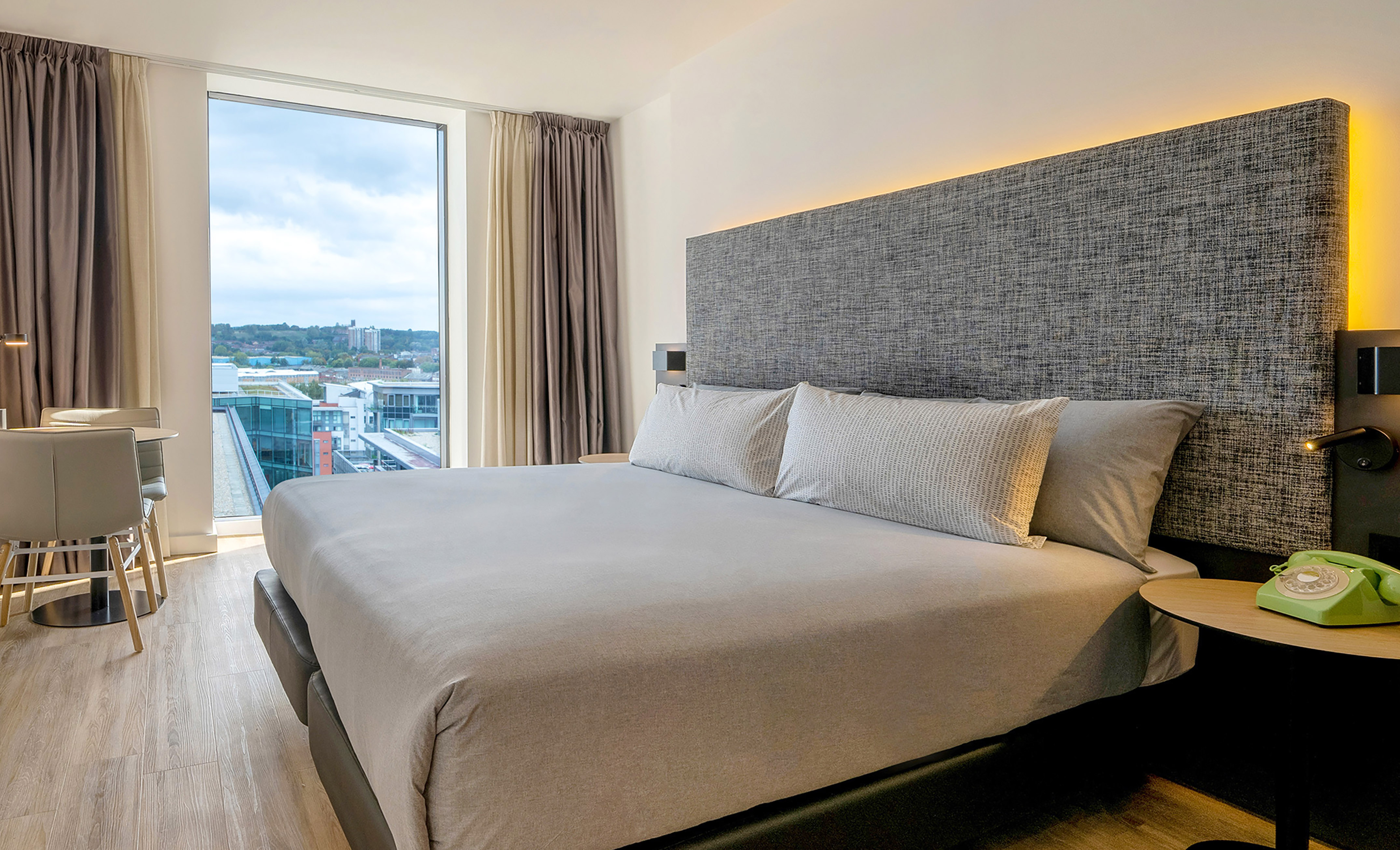 Modern hotel room with large bed, backlit headboard, and panoramic city view.