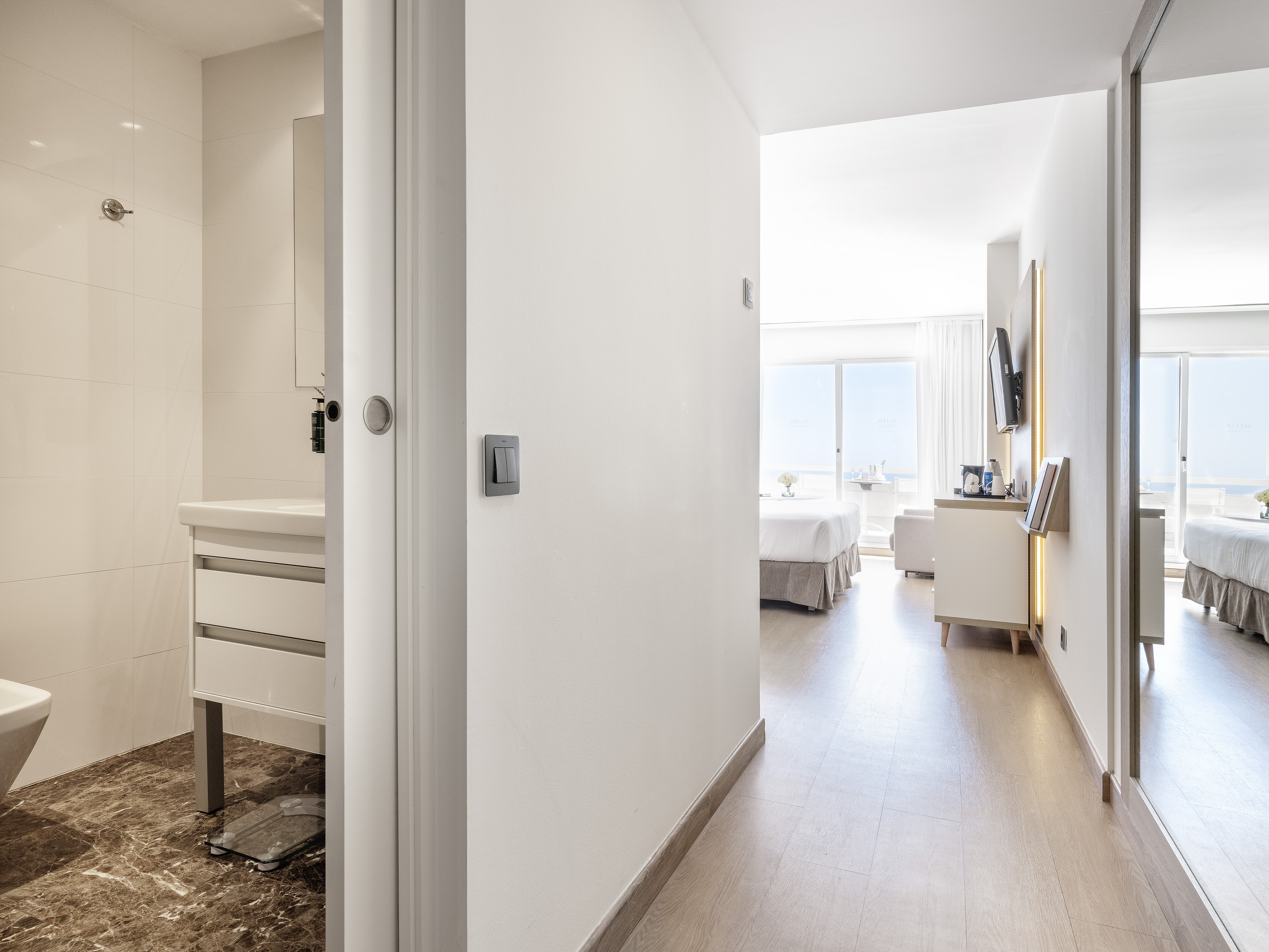 Modern hotel suite hallway leading to bright bedroom and adjacent bathroom.
