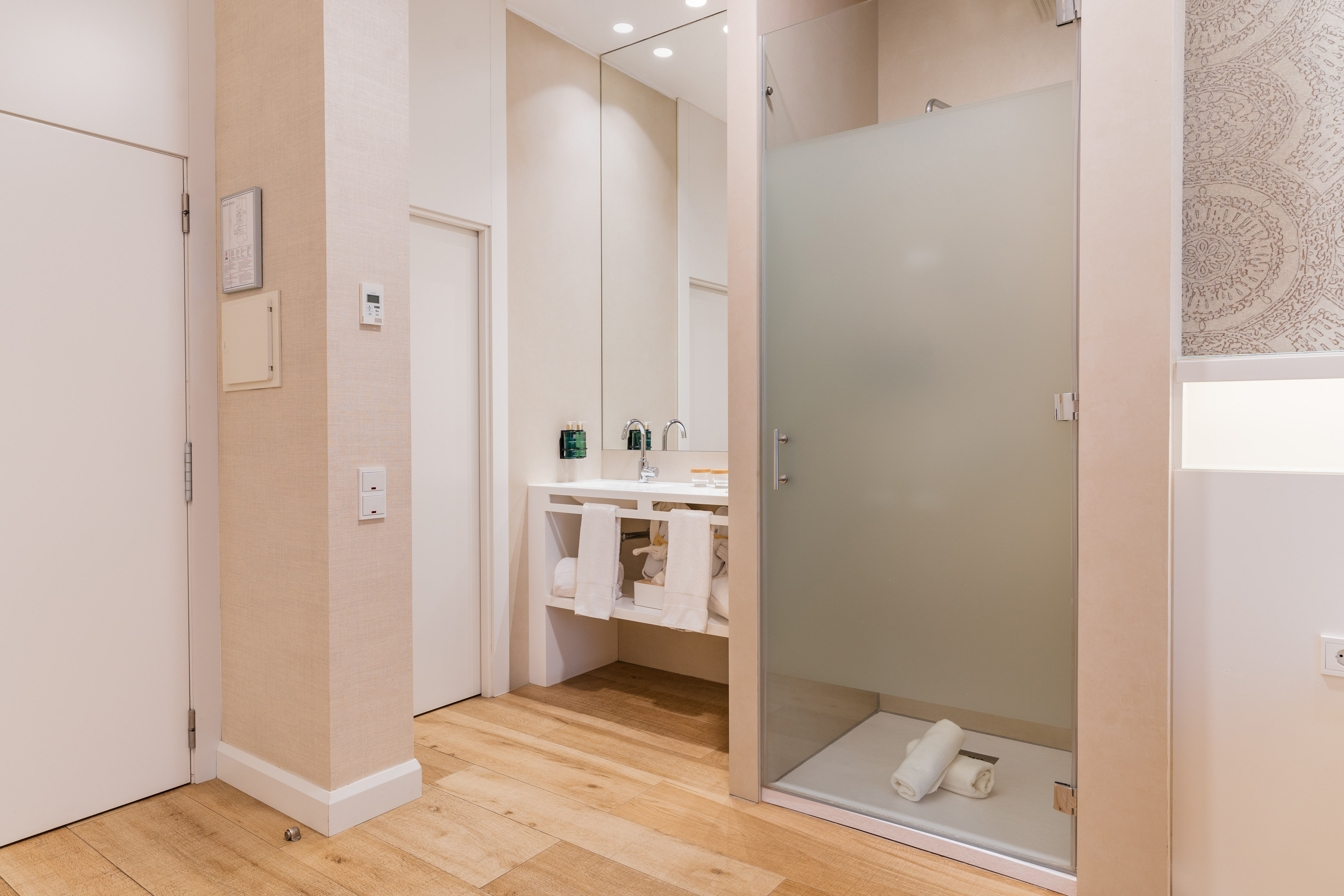 Modern hotel bathroom with wood floor, white vanity, and frosted glass shower.