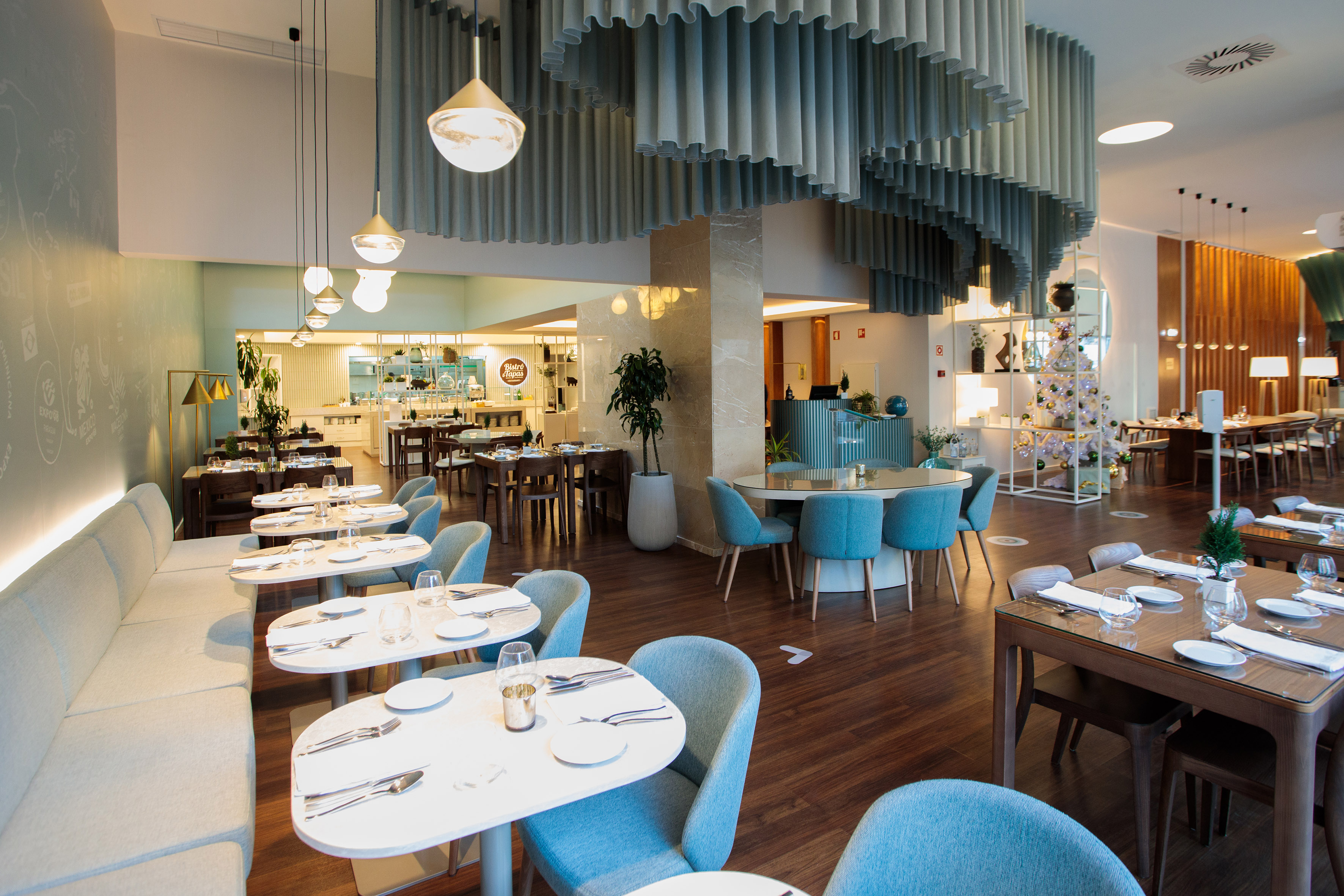 Modern restaurant interior with blue seating, wood floors, and wavy ceiling design.