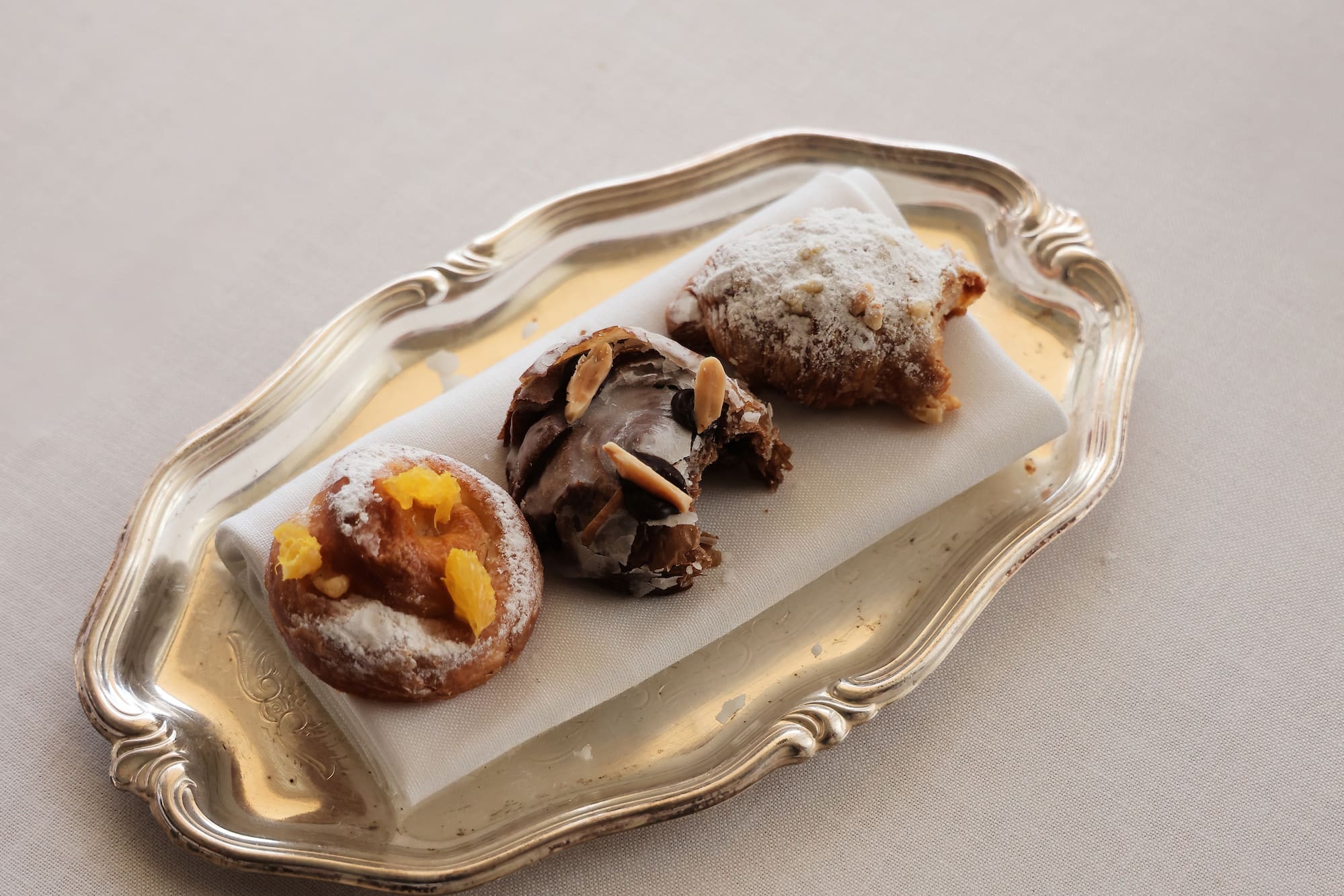 Assorted sweet pastries on a silver tray: orange, chocolate, and powdered sugar.
