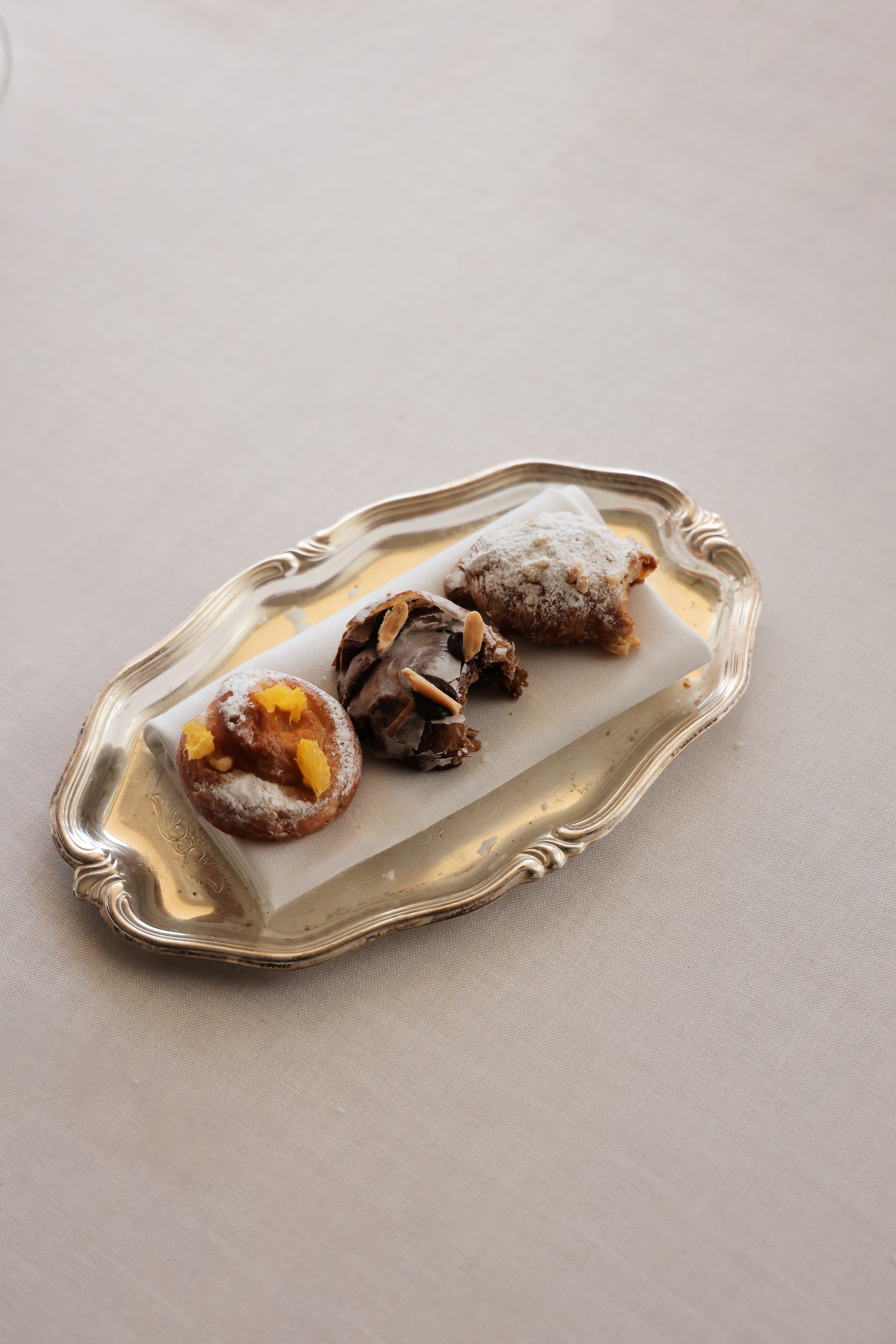 Assorted sweet pastries on a silver tray: orange, chocolate, and powdered sugar.