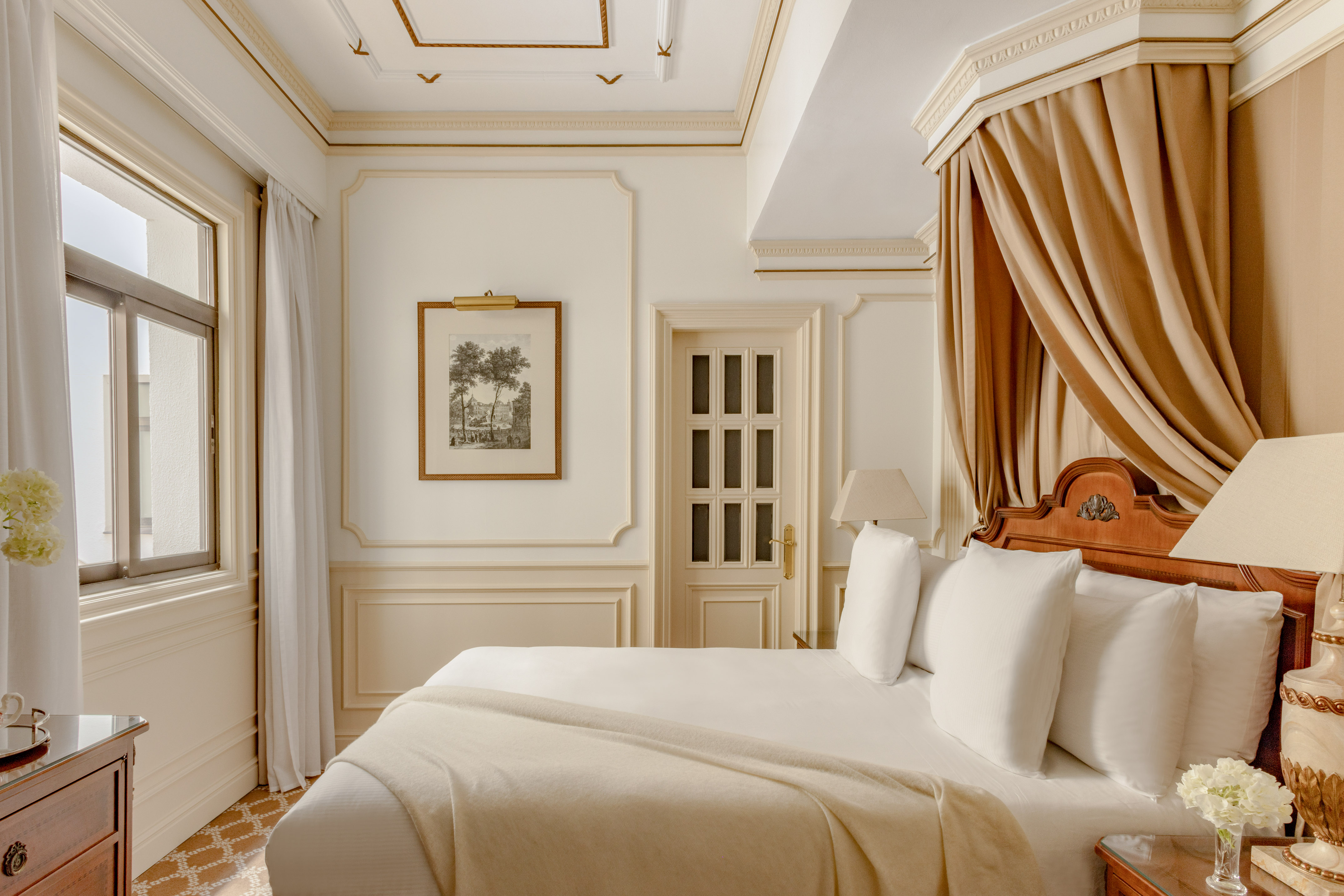 Elegant hotel room with canopy bed, white bedding, and ornate cream walls.