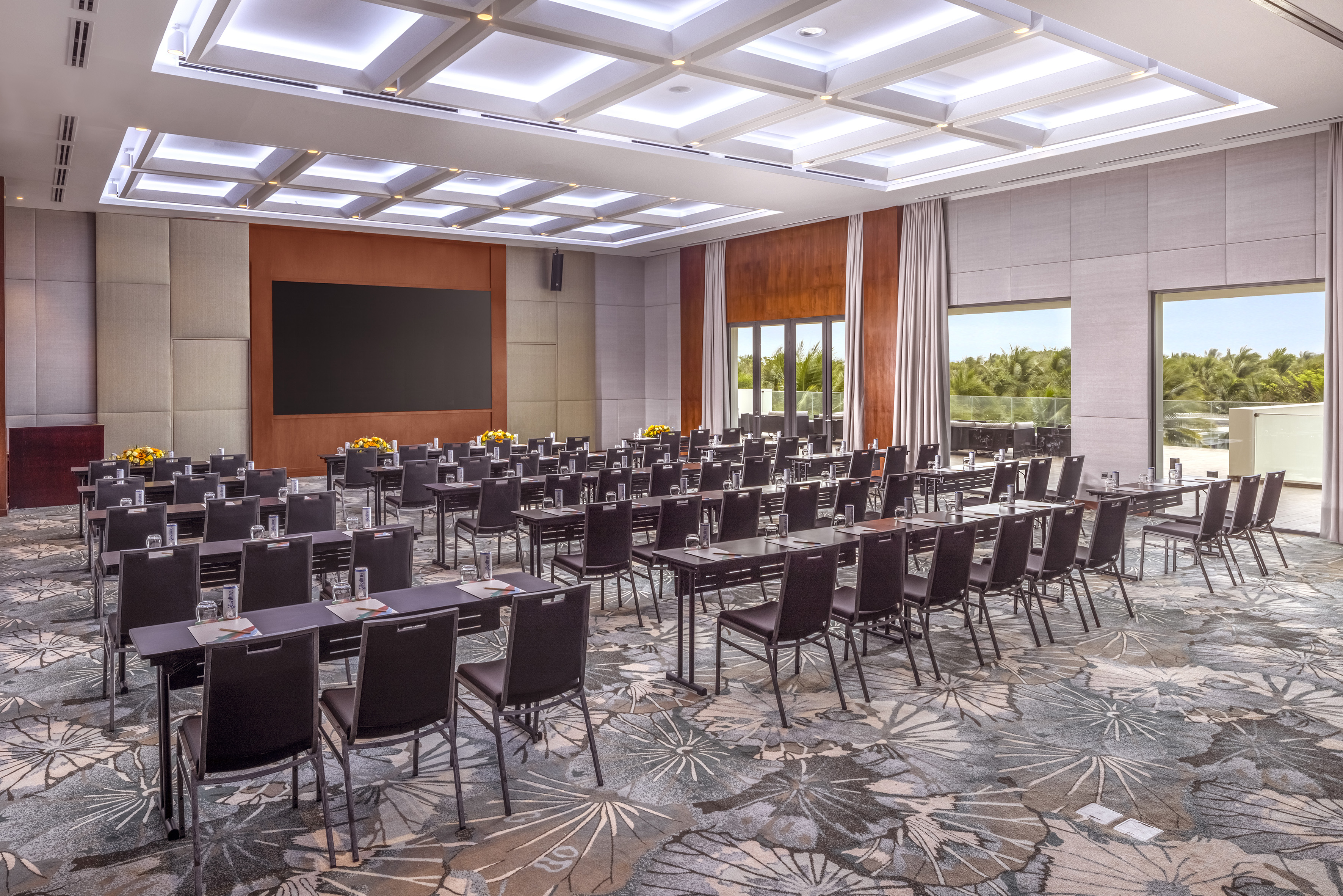 Hotel conference room with classroom setup, large screen, and tropical view.