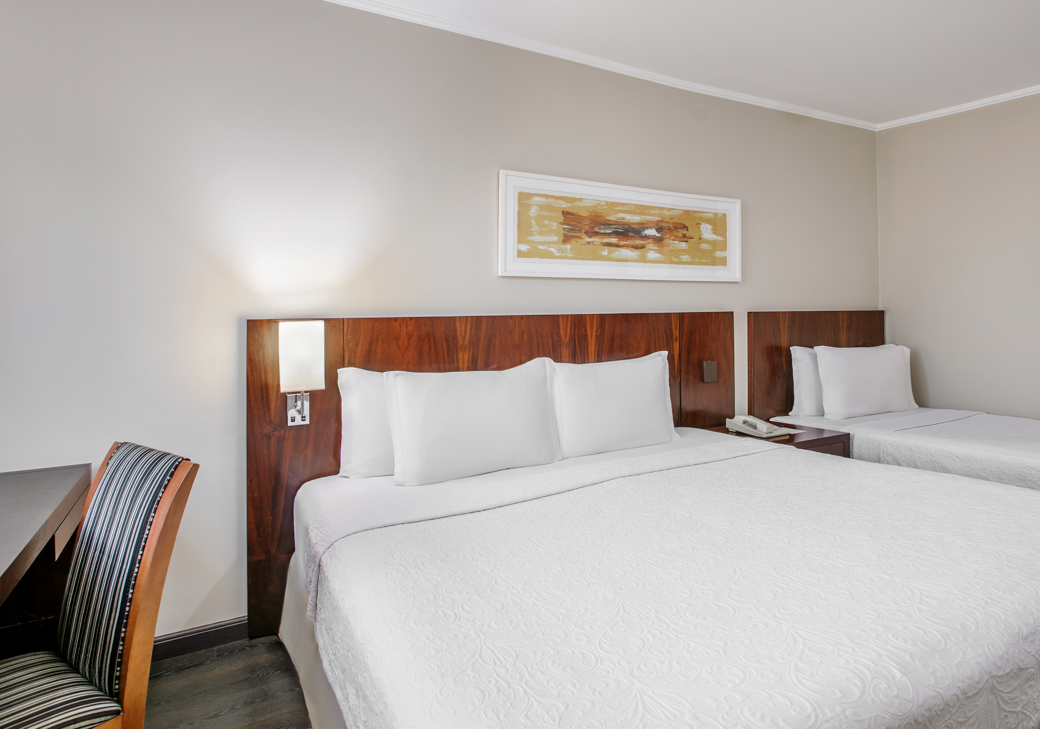 Hotel bedroom with two beds, white linens, wooden headboards, and desk.