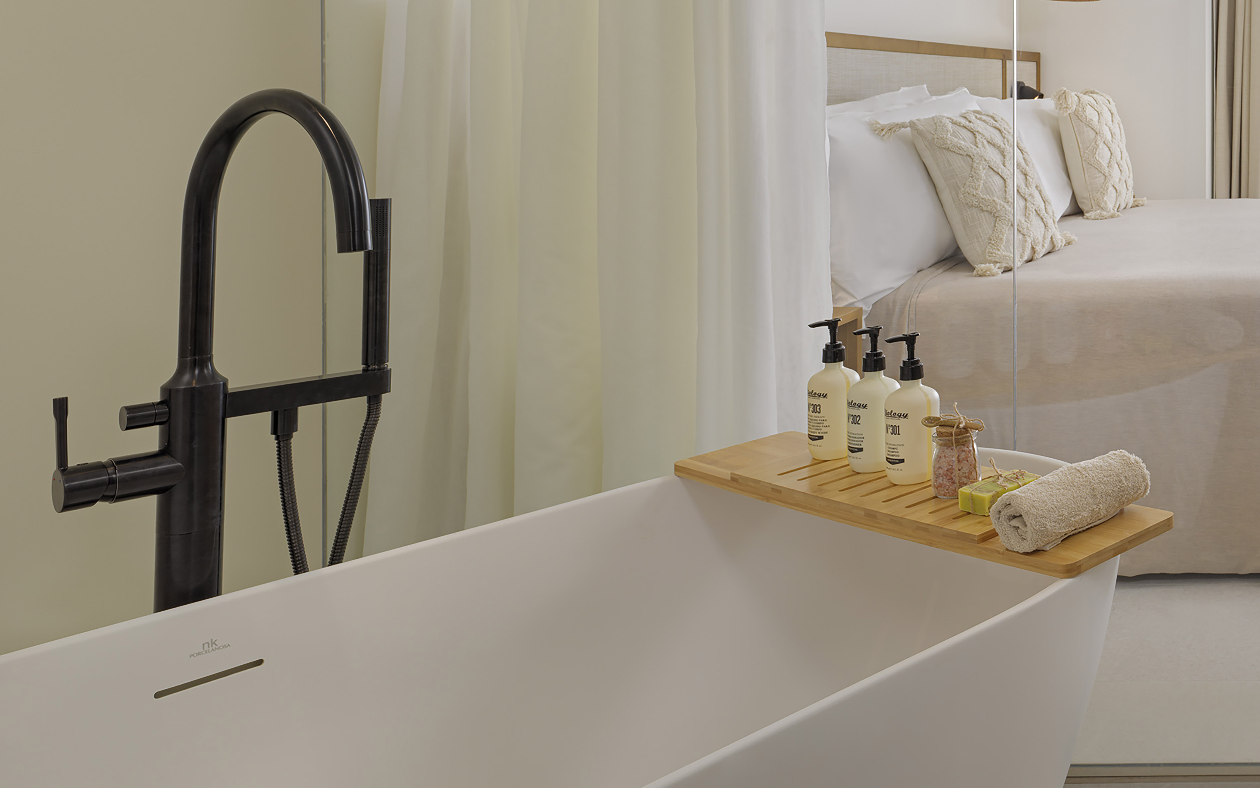 Freestanding bathtub, black modern faucet, toiletries, bamboo tray. Hotel room.