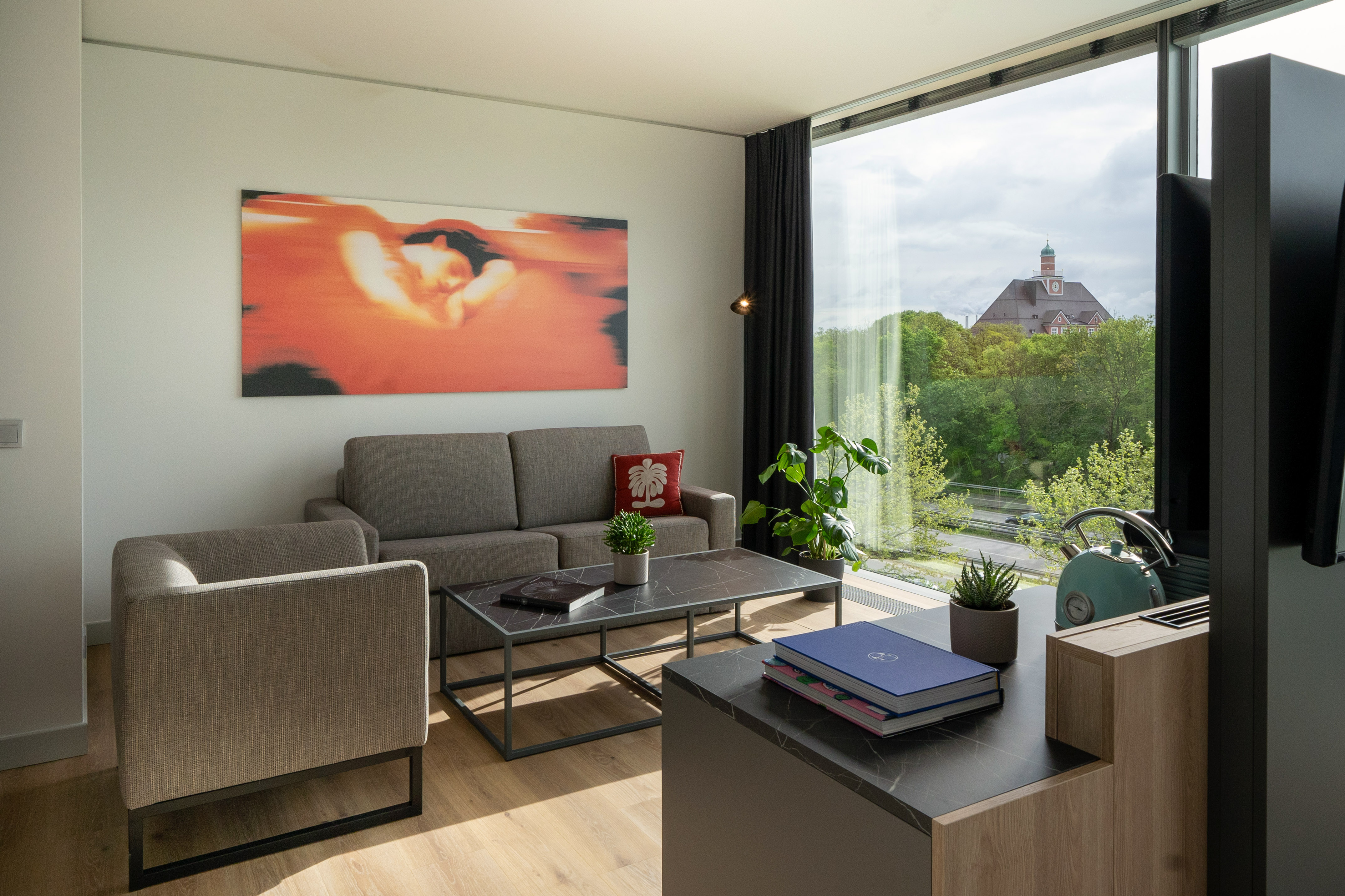 Modern living room with sofa, abstract art, coffee table, and large window city view.