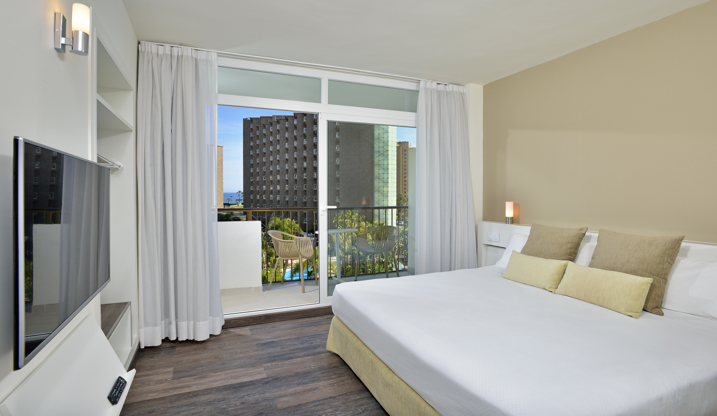 Modern hotel room with bed, private balcony, and ocean city view.
