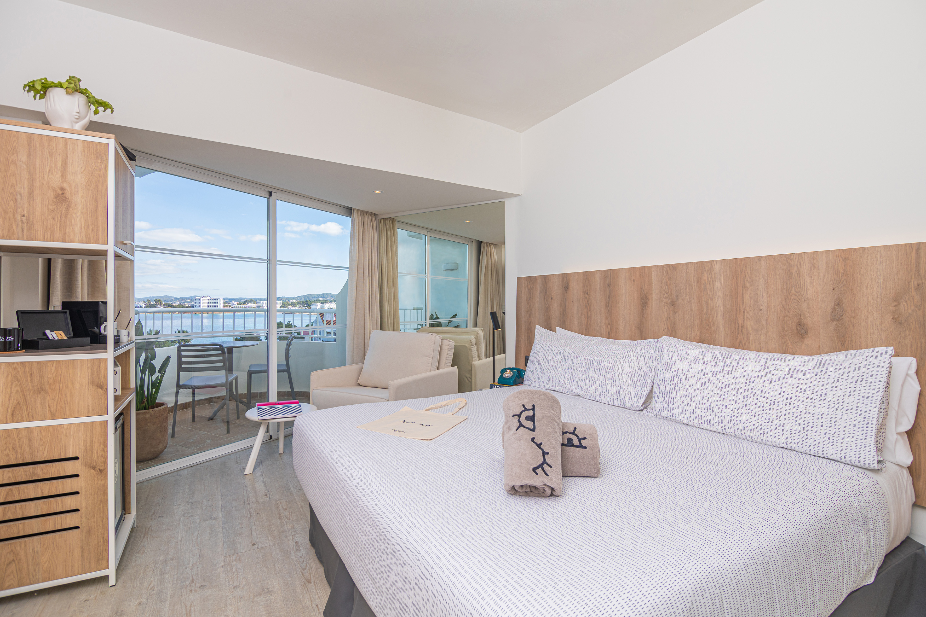 Modern hotel room with ocean view balcony, large bed, and light wooden furniture.