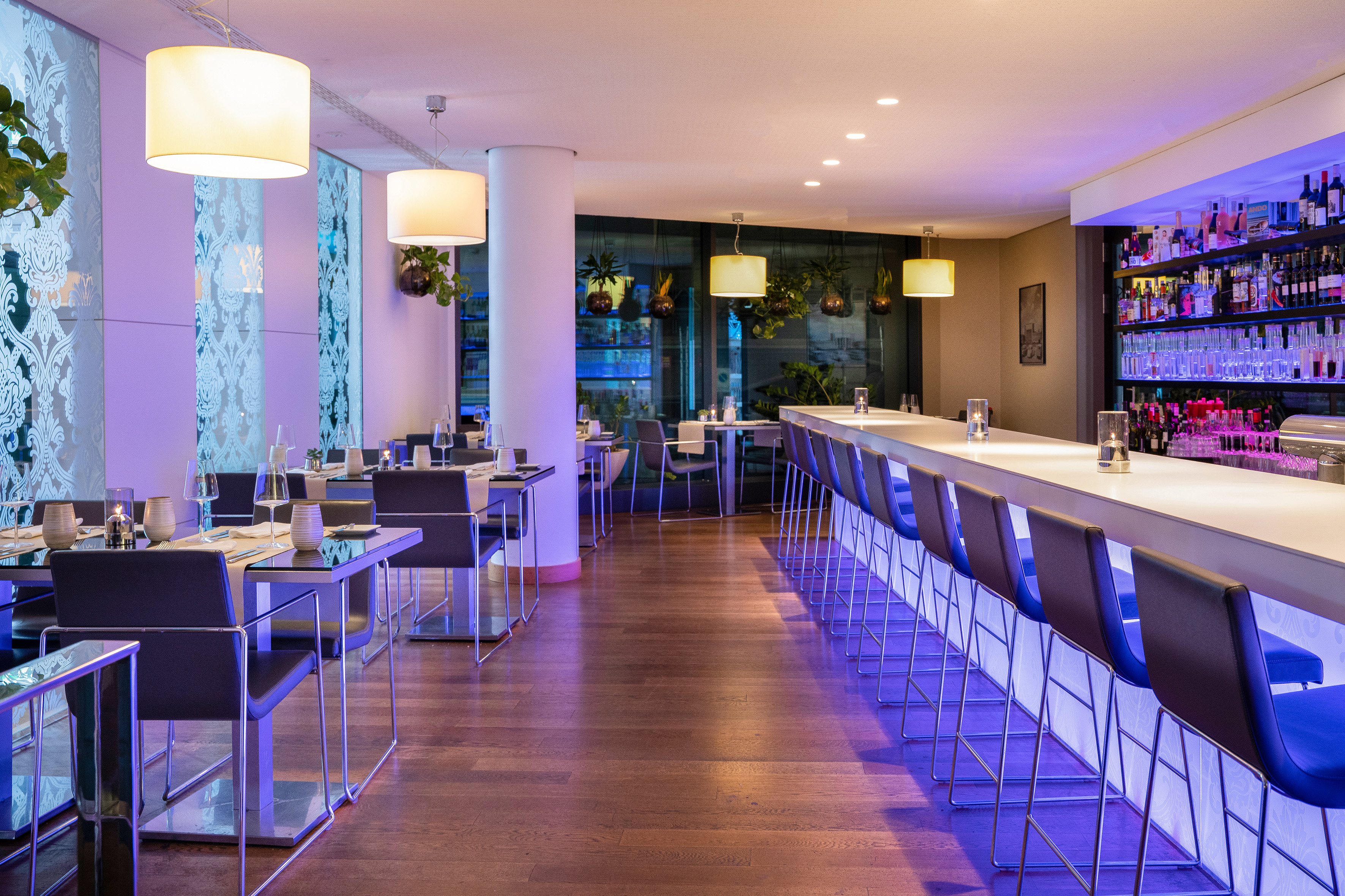 Modern restaurant and bar interior with dining tables, long bar, and purple ambient lighting. - VEN, Bucătărie internațională - Innside Dresda, Dresda